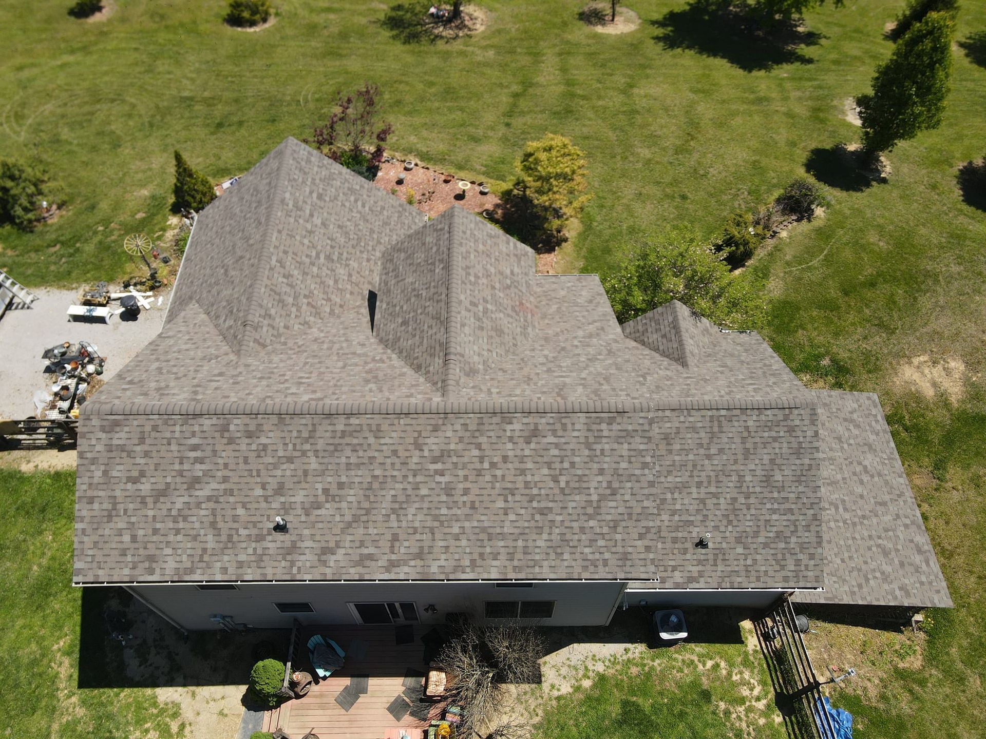 An aerial view of a house with a gray roof surrounded by grass and trees.