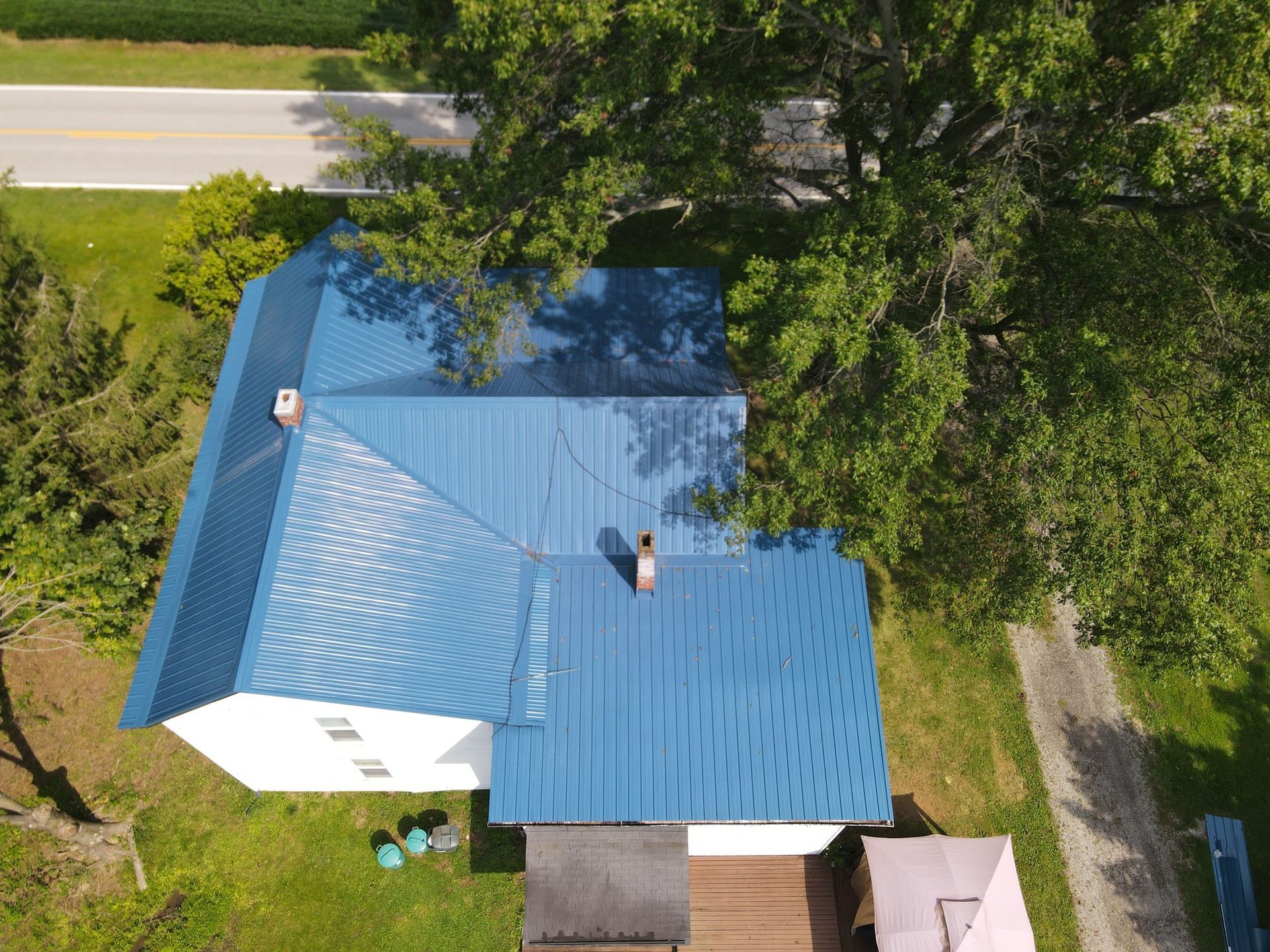 An aerial view of a blue roof of a house surrounded by trees.