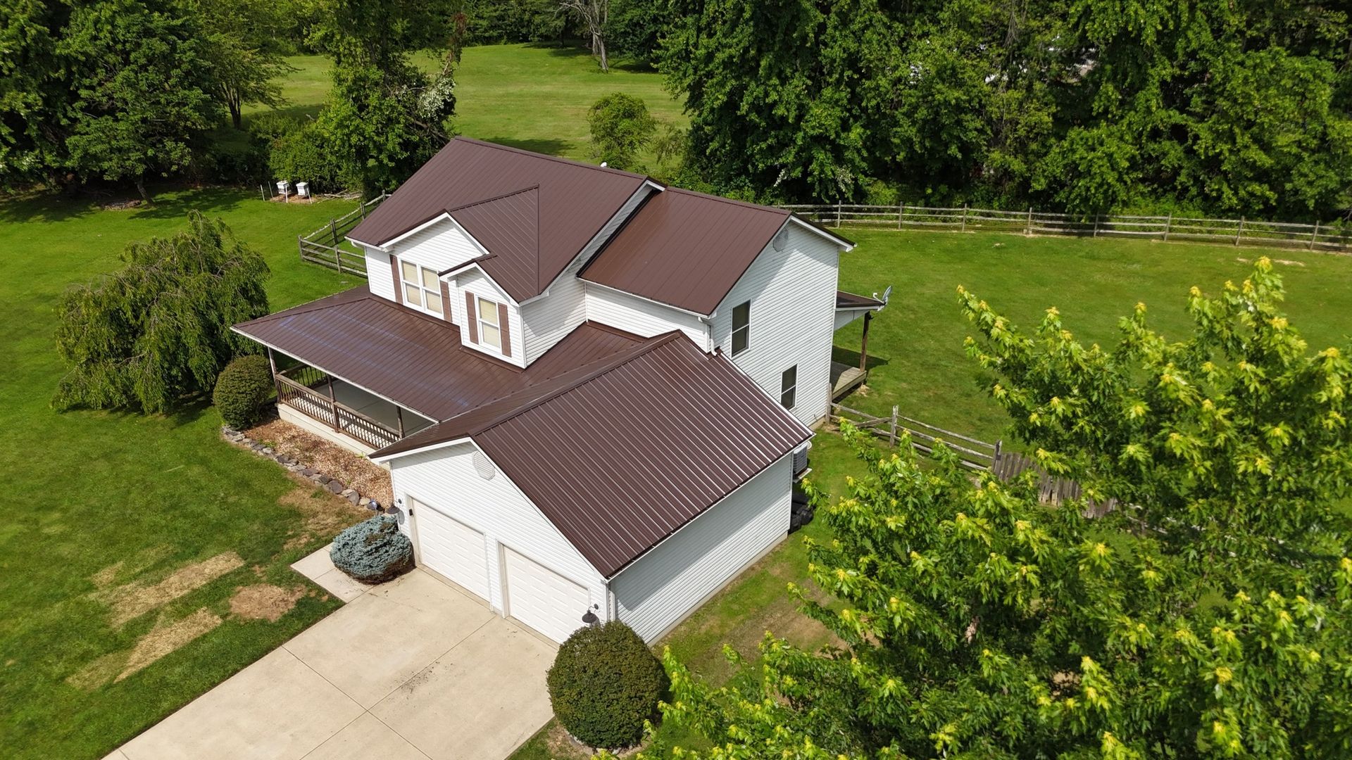 An aerial view of a white house with a brown roof surrounded by trees.