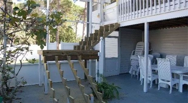 Wooden outdoor staircase leading to a second-story deck. White siding, dining table, chairs underneath.