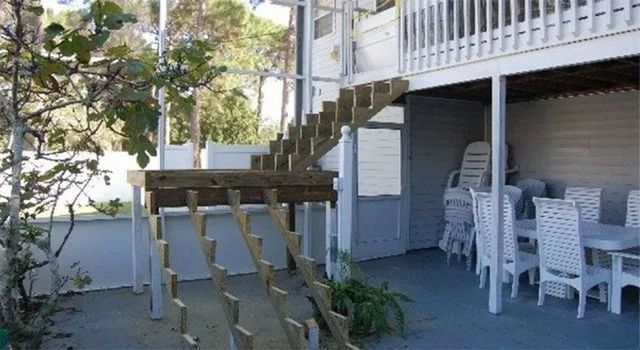 Wooden outdoor staircase leading to a second-story deck. White siding, dining table, chairs underneath.