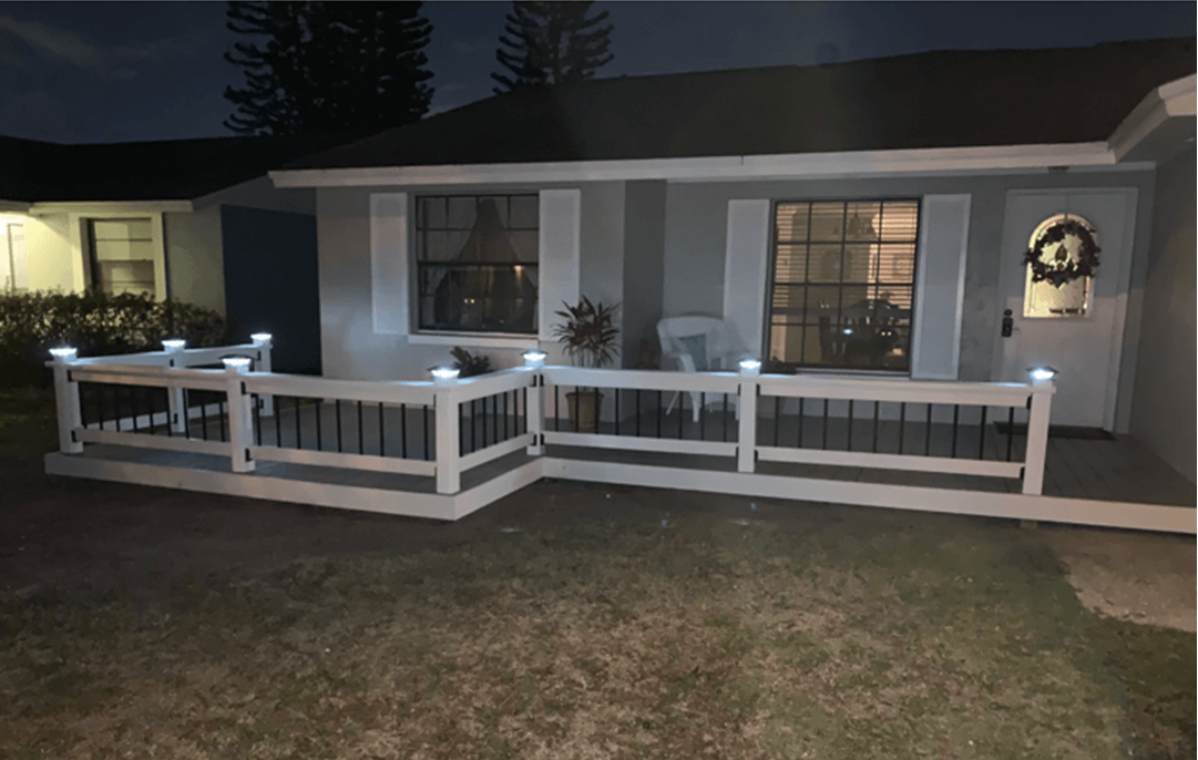 A house with a white fence, porch, and solar lights at night.