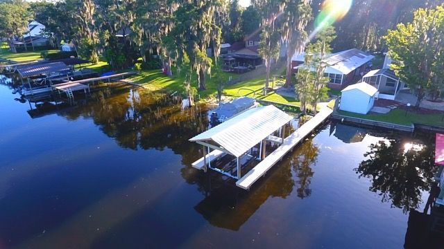 Aerial view of a boat dock on a dark lake, with houses and trees lining the shore.