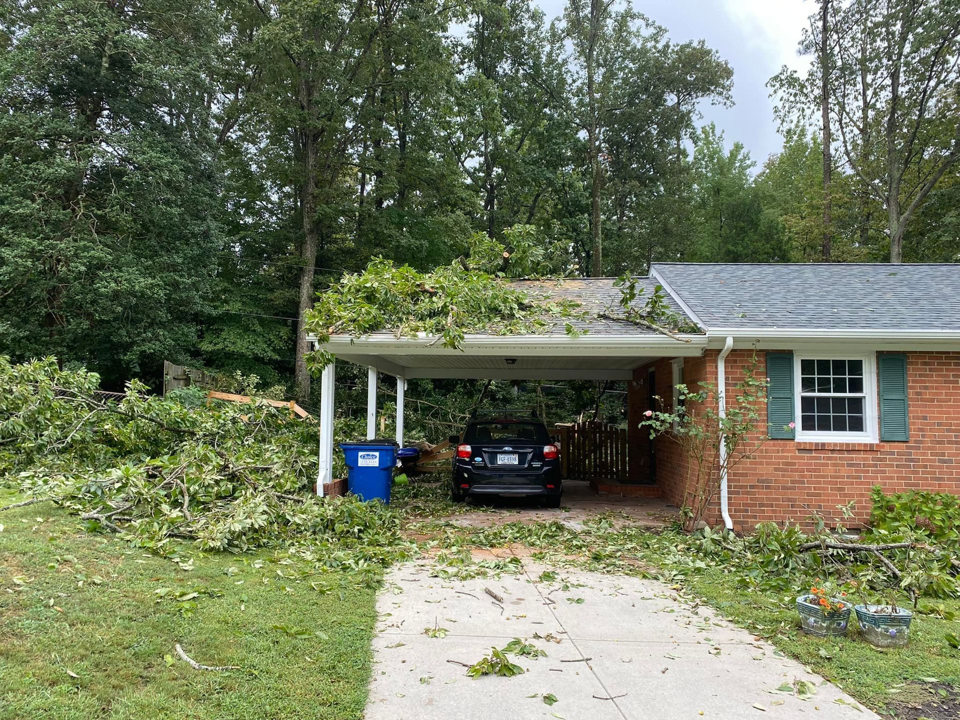 A car is parked under a carport in front of a brick house.