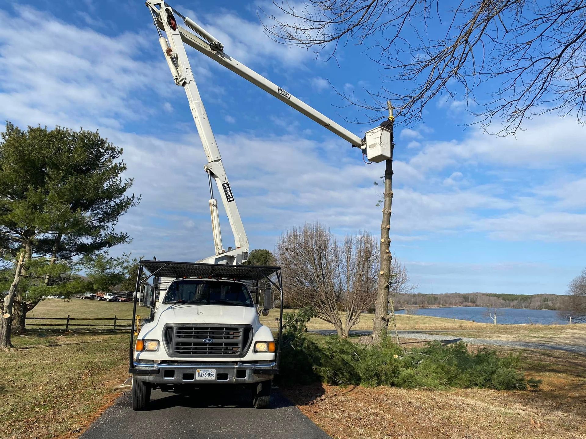 A white truck with a crane on top of it is parked next to a tree.