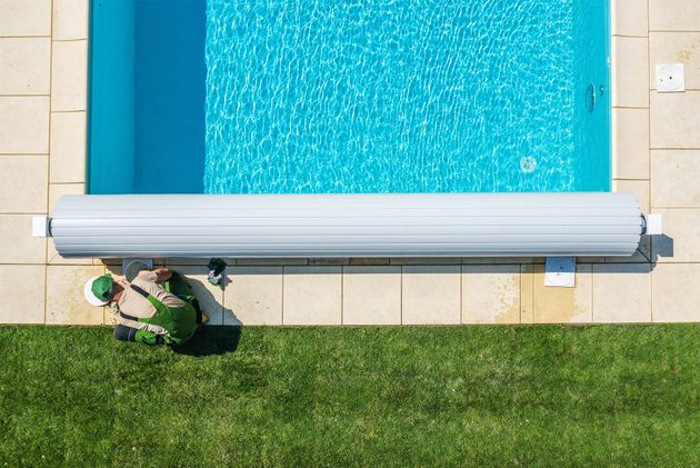 Aerial view of a backyard pool with a person on a lounge chair beside the patio and lawn.