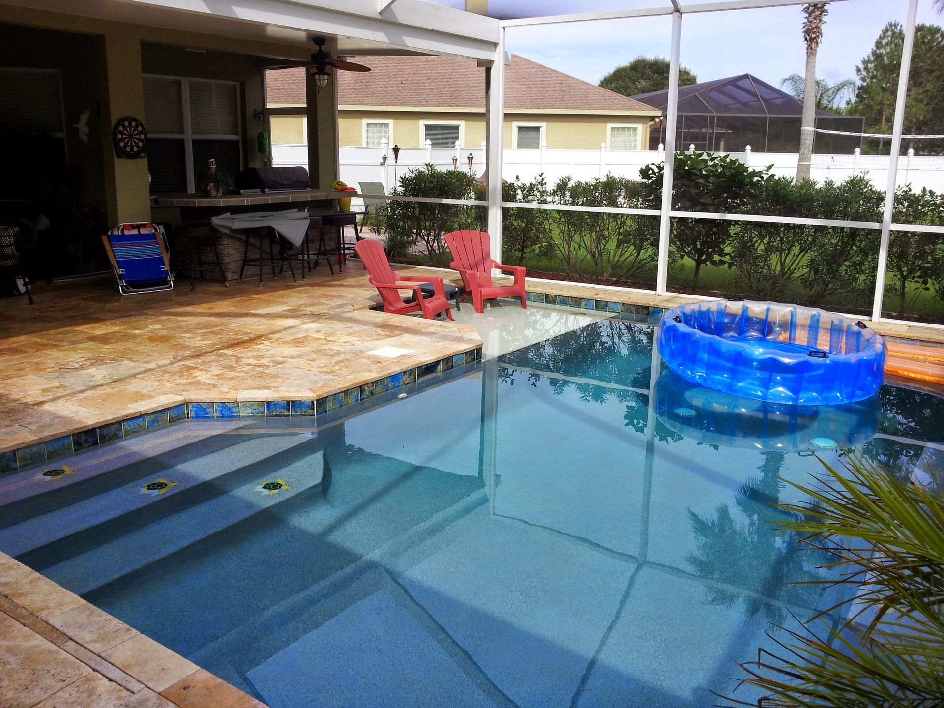 Backyard swimming pool with a blue inflatable float and red chairs on a covered patio