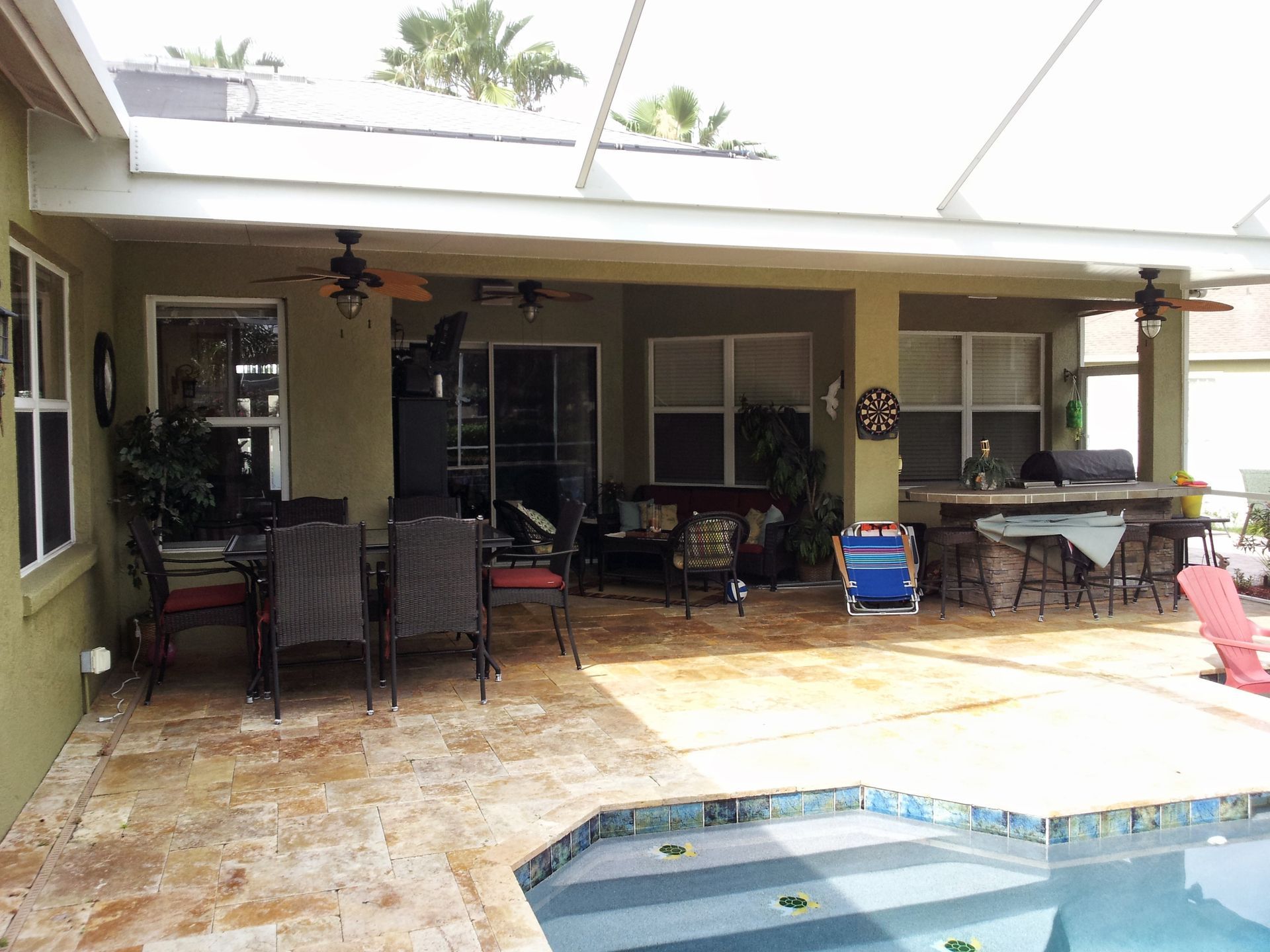Covered patio with wicker furniture beside a small pool, tiled floor, and sliding glass doors.