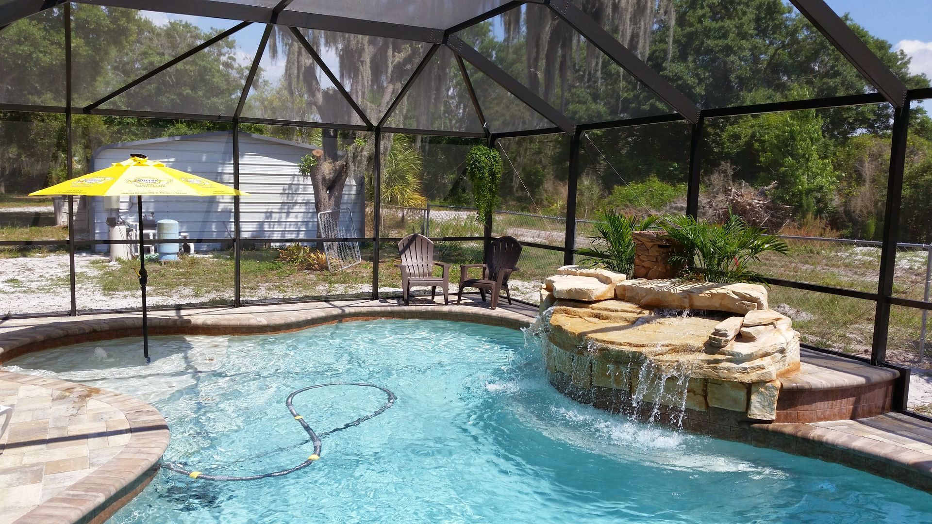 Screened-in backyard pool with a stone waterfall and yellow umbrella in the background