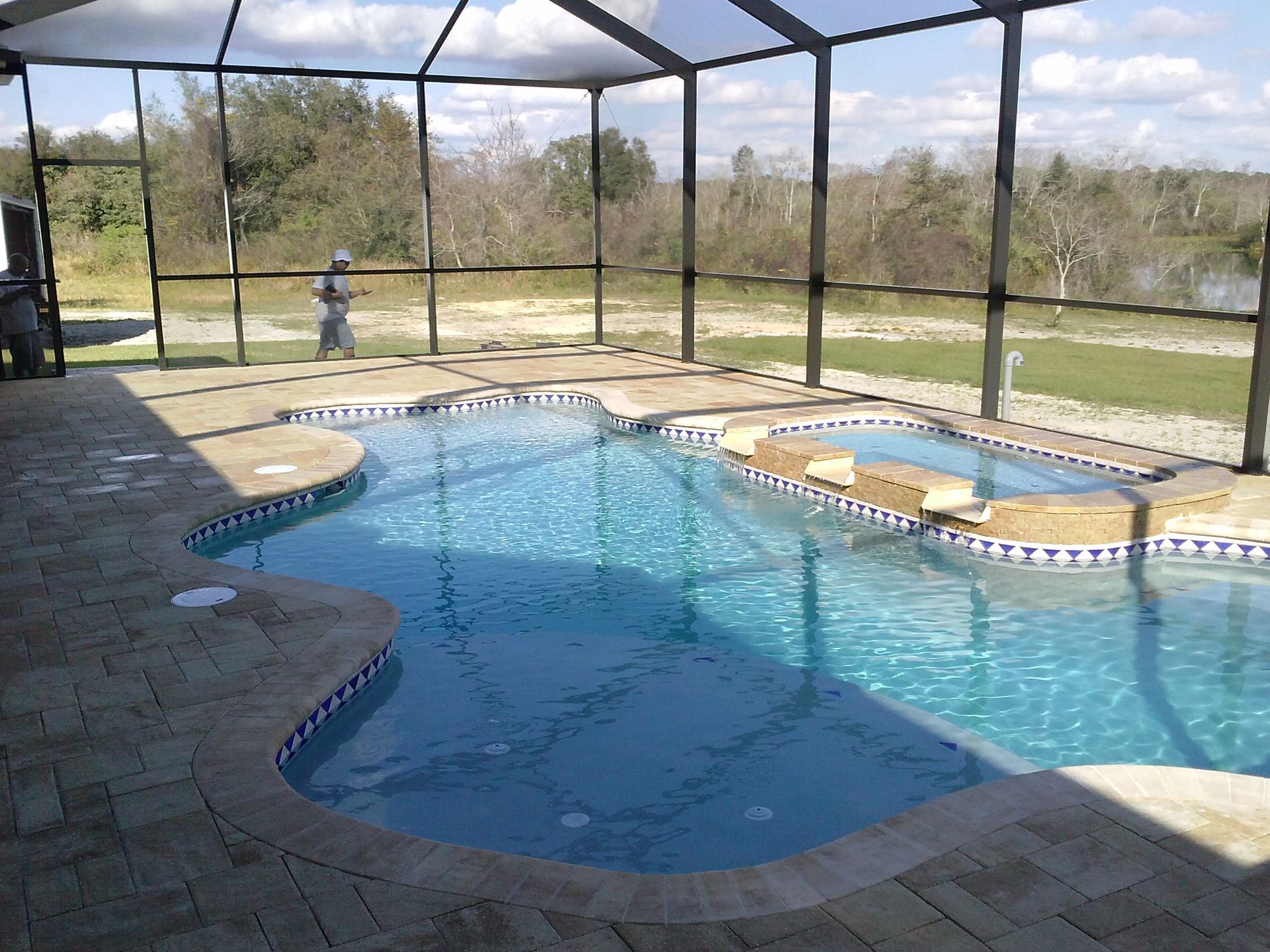 Covered backyard swimming pool with blue water, screened enclosure, and patio seating area