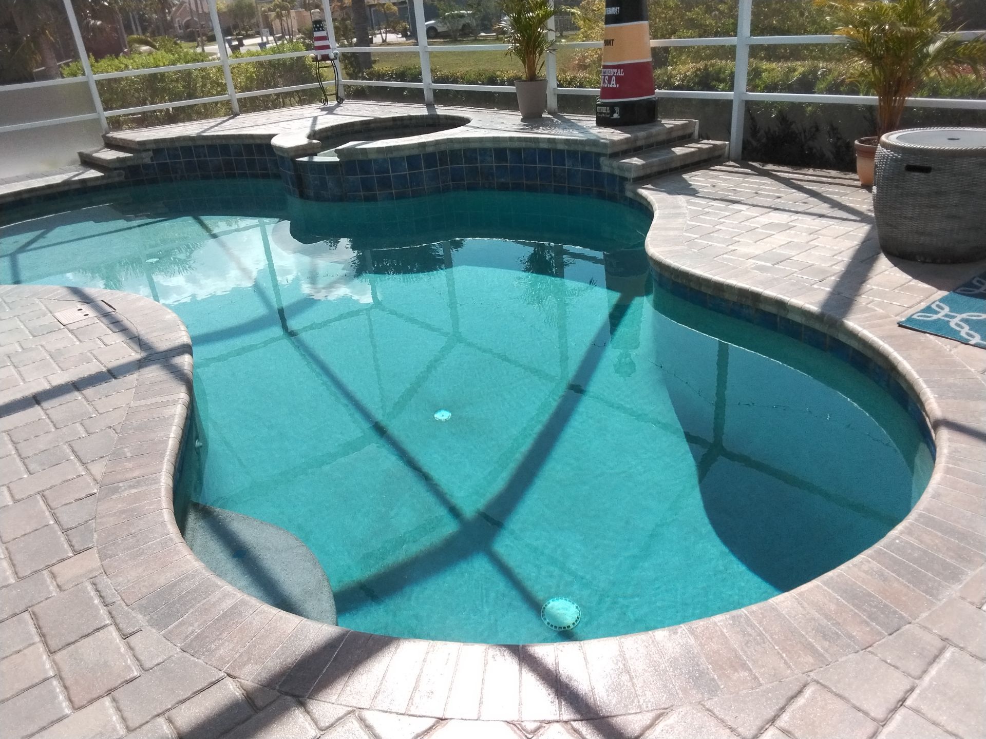 Backyard swimming pool with curved turquoise water and stone patio in bright sunlight.
