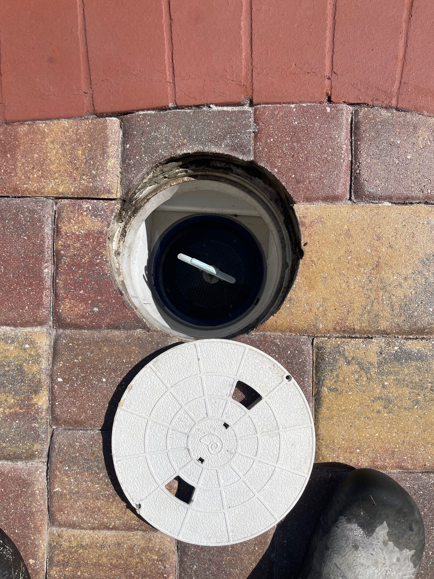 Open round wall vent with black interior above a white circular cover on a brick wall.