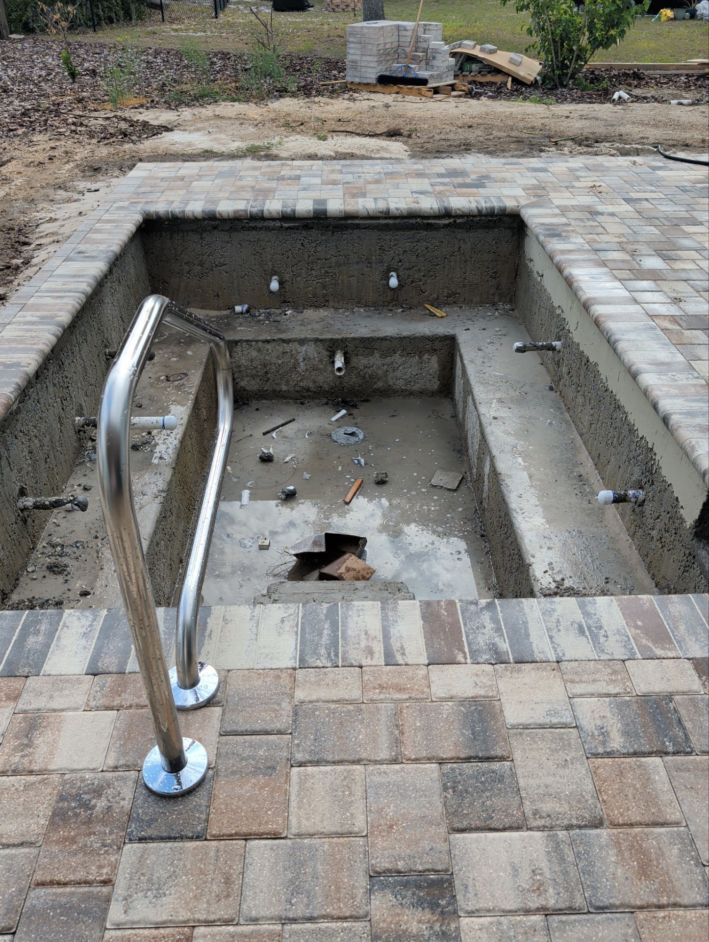 Empty in-ground spa or small pool with a stainless steel handrail and paver stone surround.