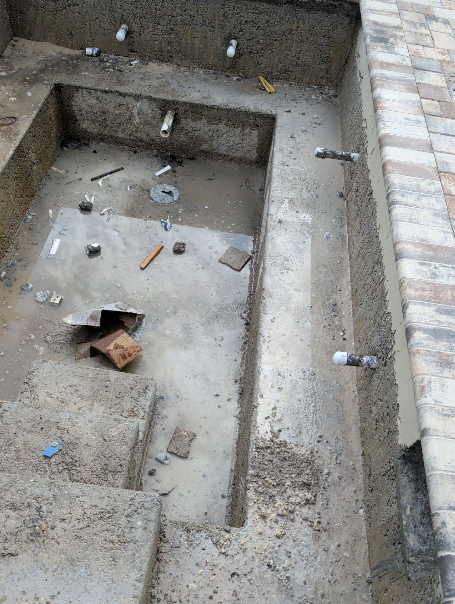 Concrete stairwell with scattered debris and trash in a narrow pit, viewed from above.