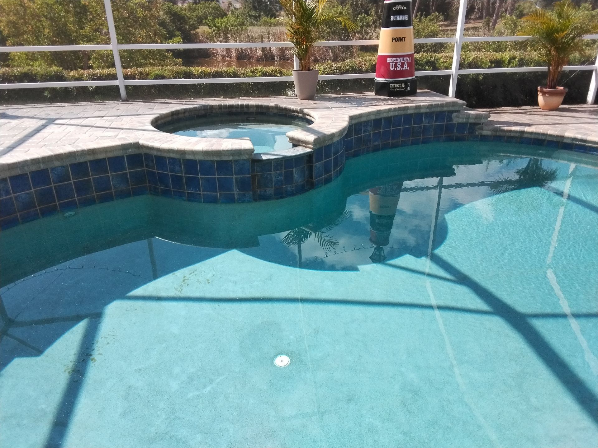 Backyard swimming pool with blue water, curved spa, tiled deck, and potted plants in the background.