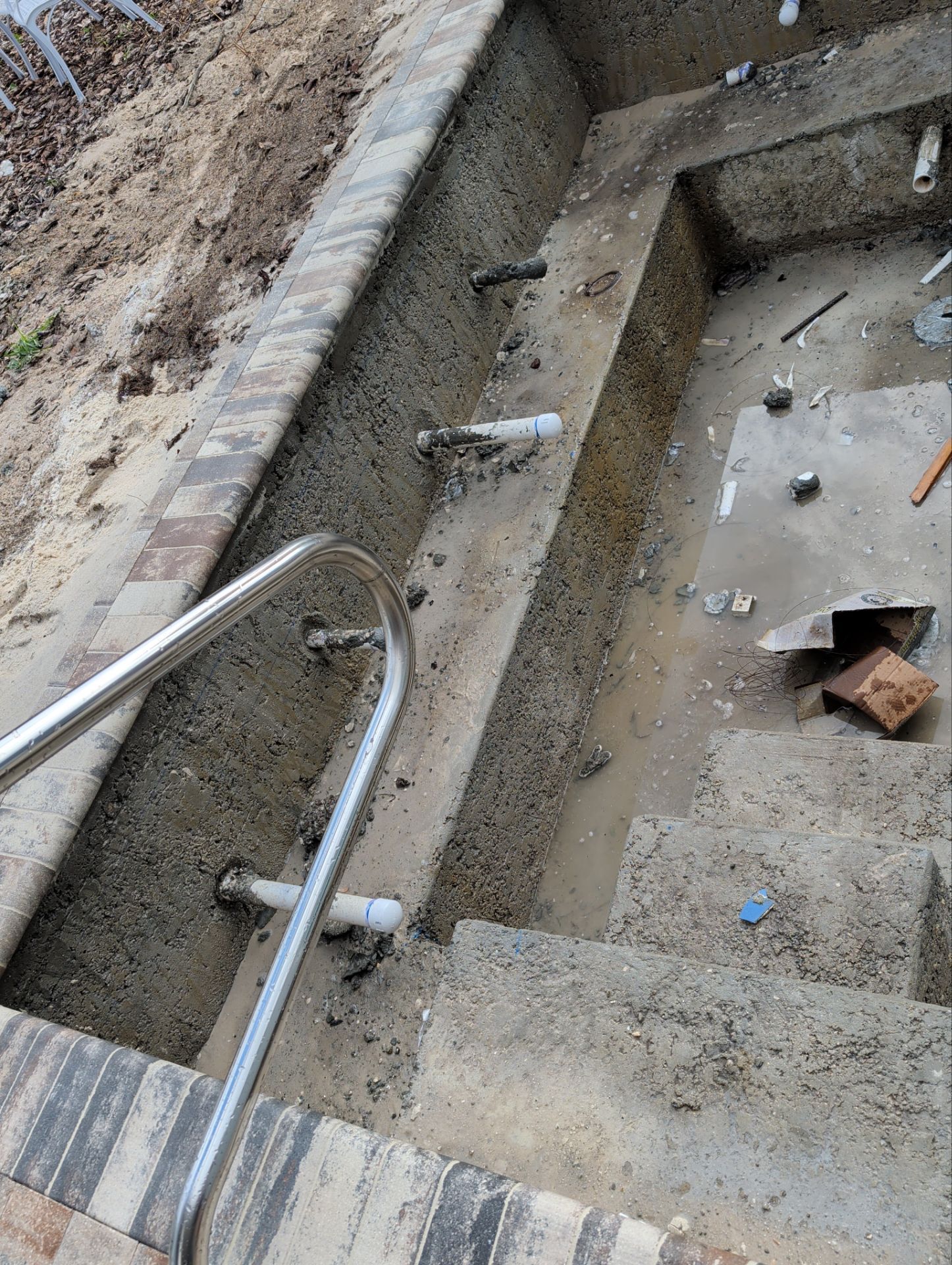 Concrete stairwell under construction with metal handrails, dirt, and scattered debris.
