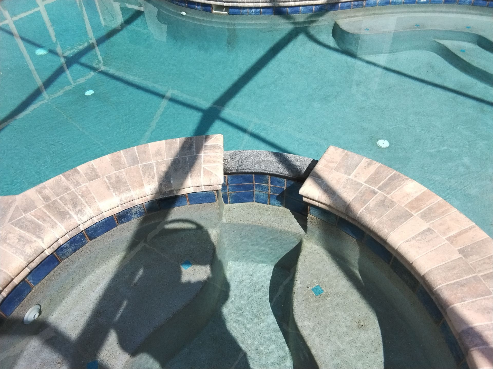 Curved stone spa with bubbling water in a turquoise swimming pool under bright sunlight.