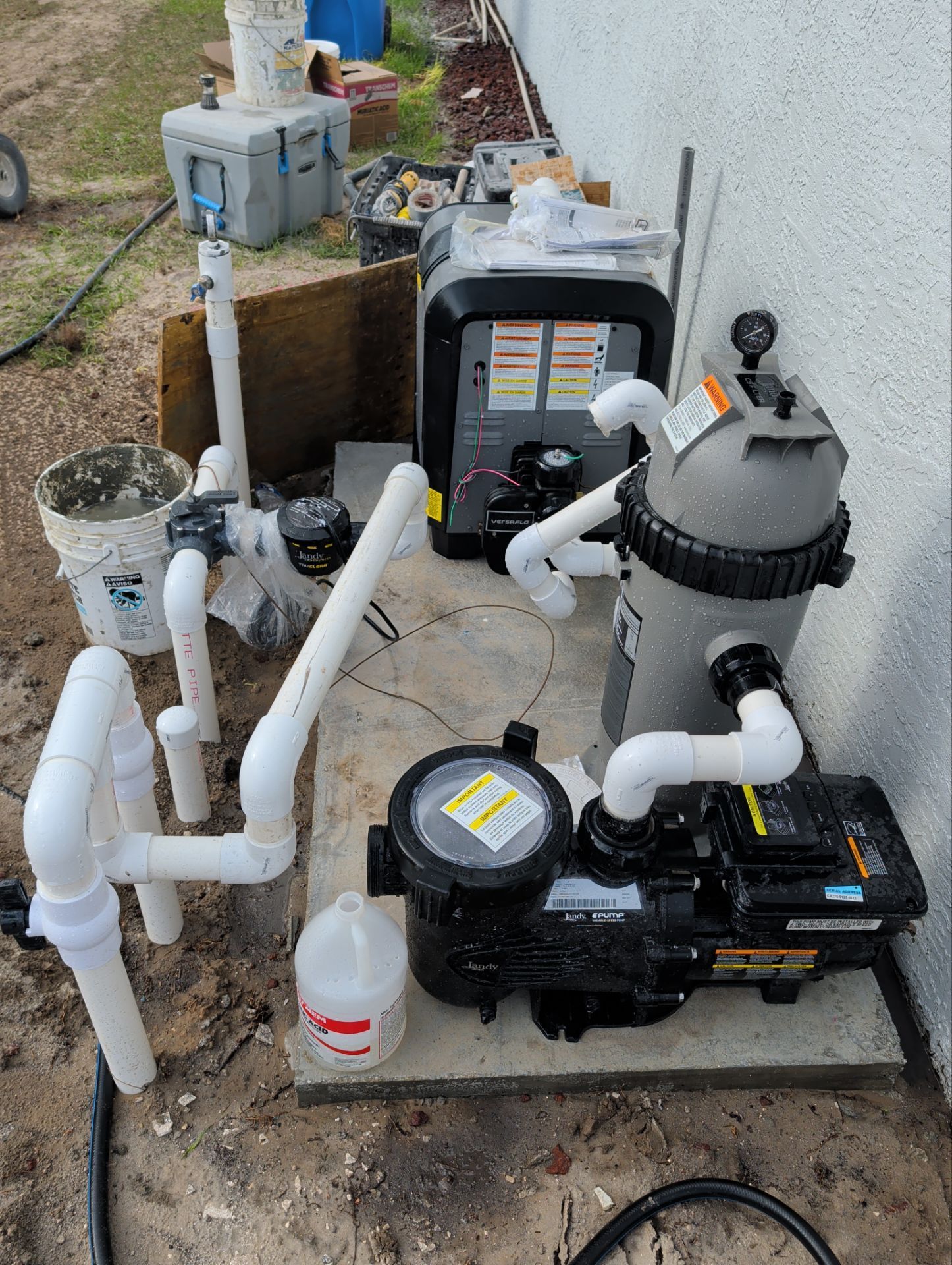 Pool pump and filter plumbing setup with white PVC pipes, black equipment, and a gray filter tank outdoors.