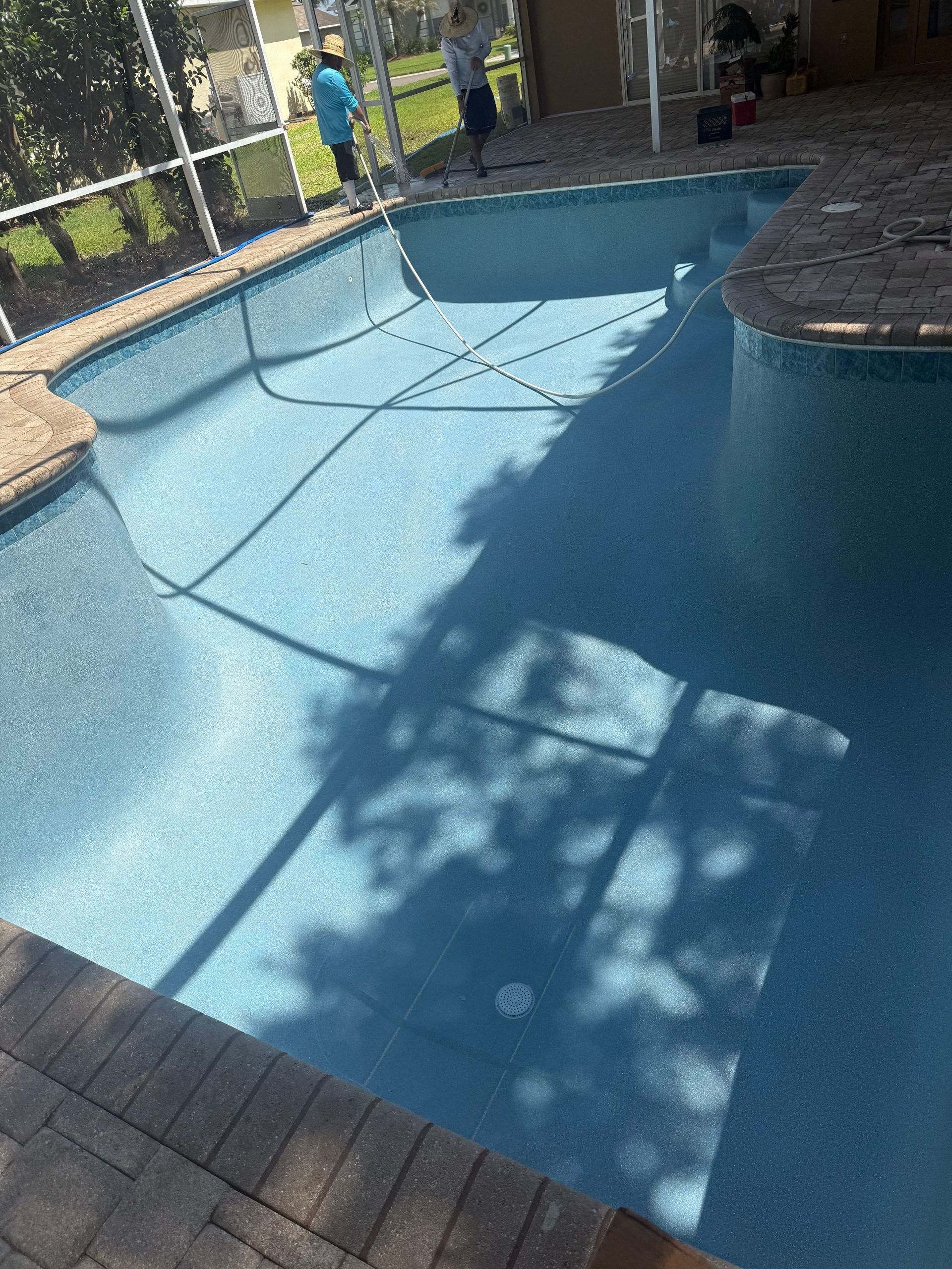 Empty blue backyard pool with a child standing by the fence.