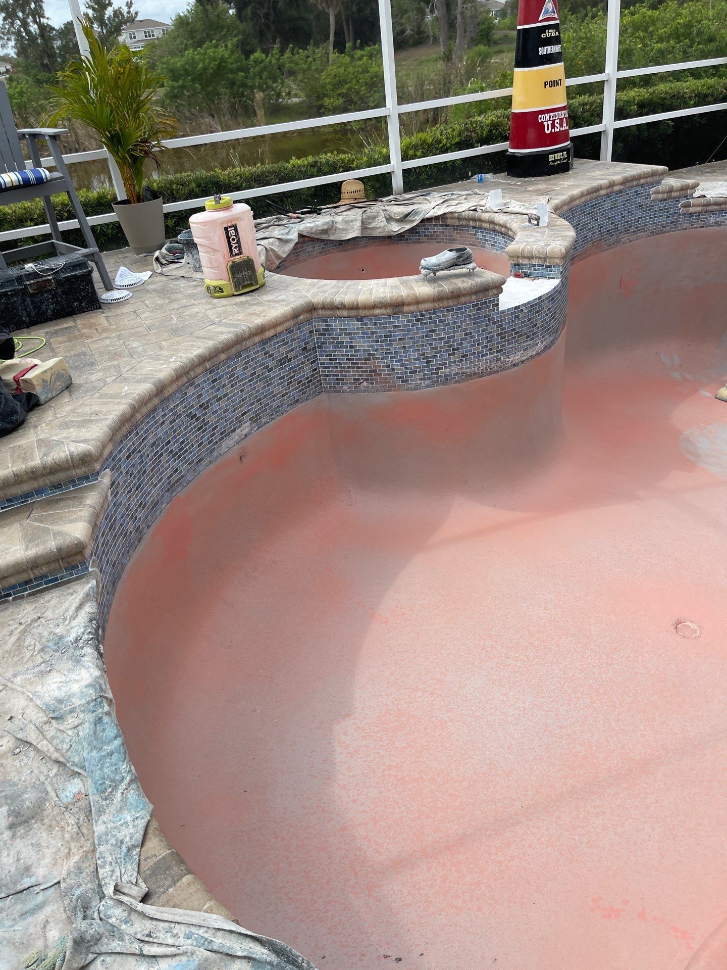 Empty pink backyard pool with a stone border and nearby steps, overlooking a fenced patio area.