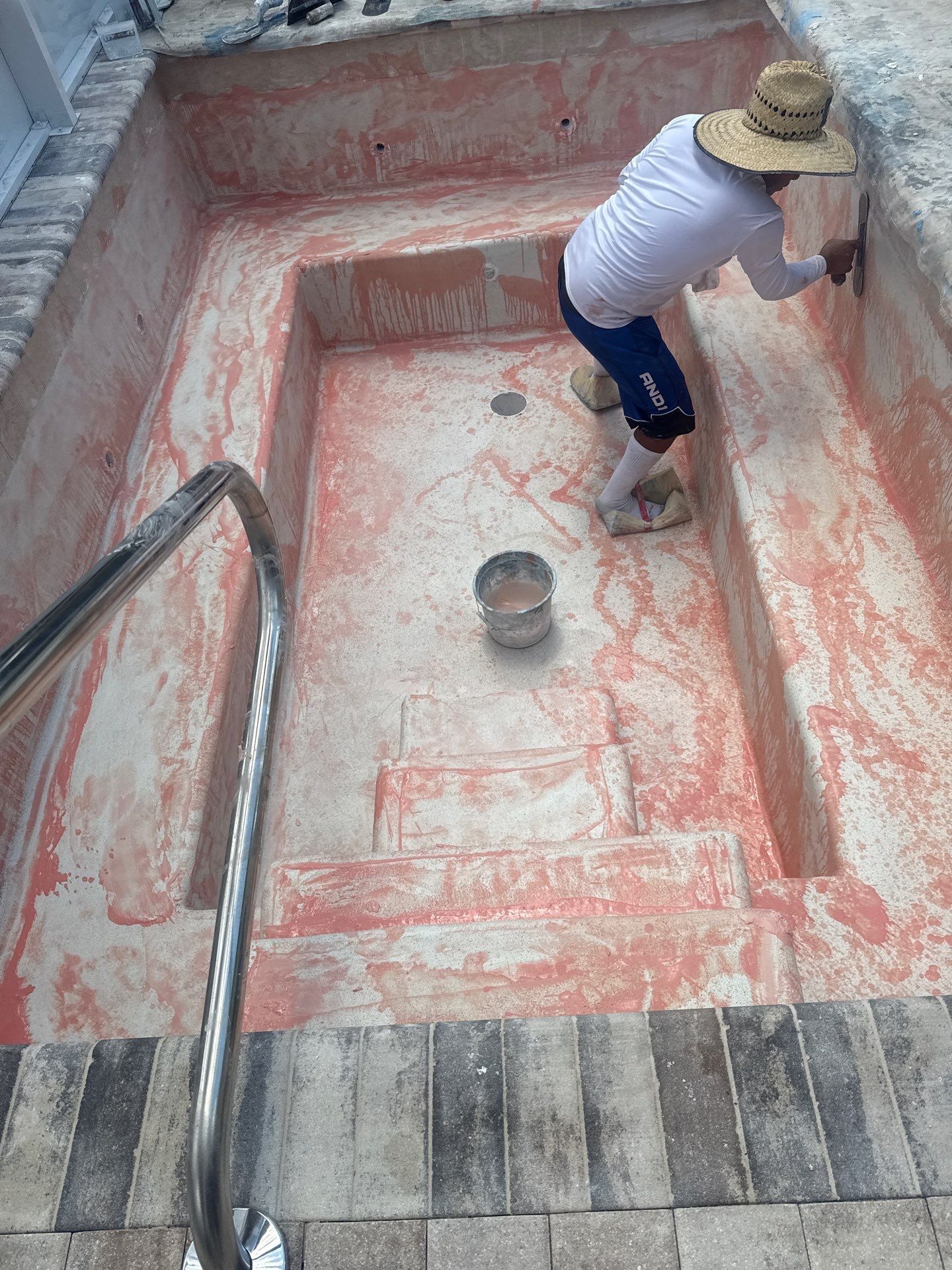 Person painting a red concrete stairwell next to gray brick steps and metal railing.