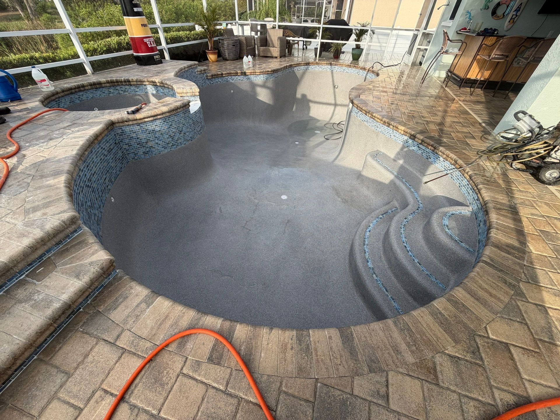Empty backyard swimming pool with dark liner, surrounded by brick pavers and a hot tub.
