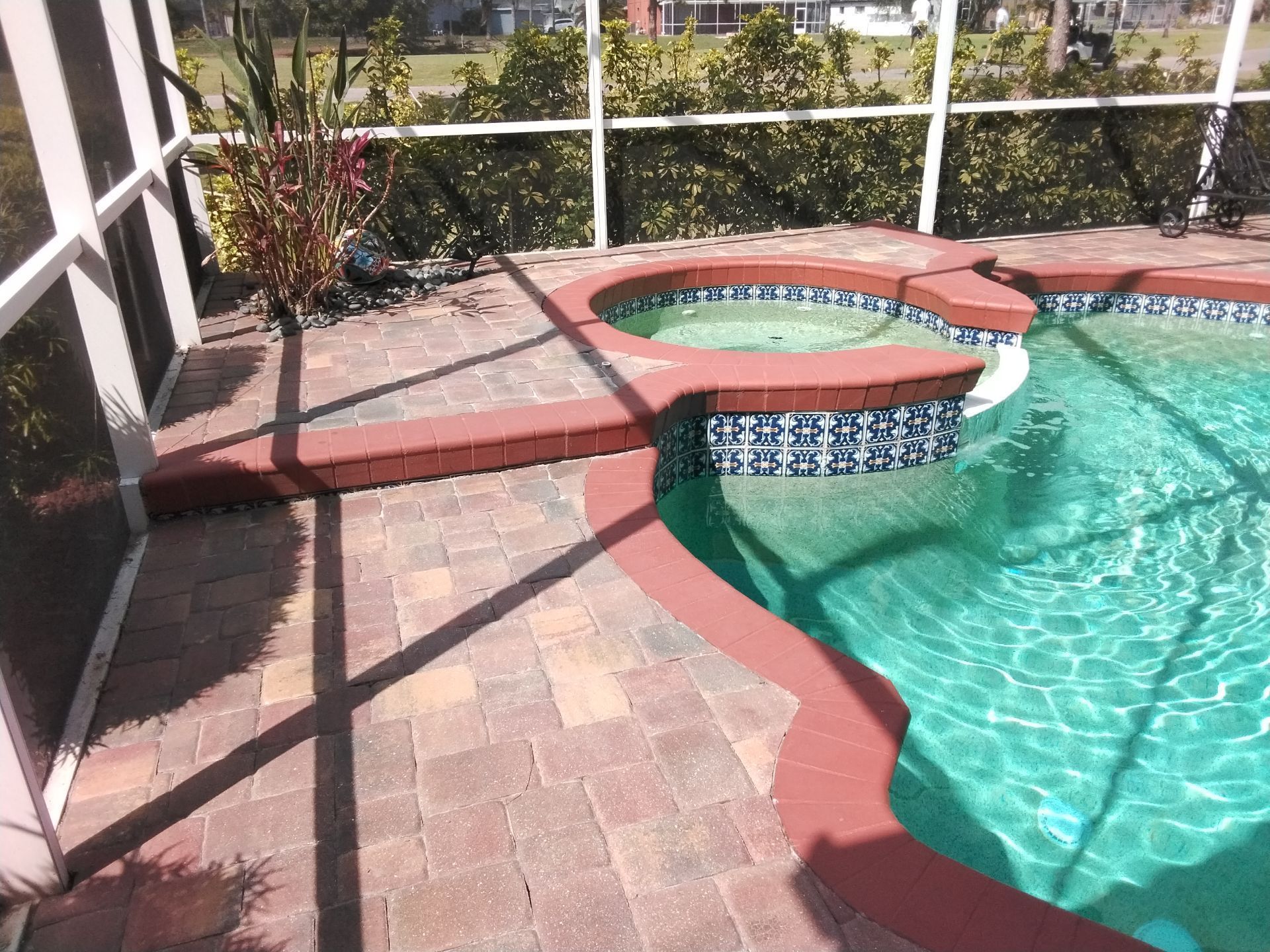 Backyard pool with a circular hot tub, red brick coping, and turquoise water under sunny light.