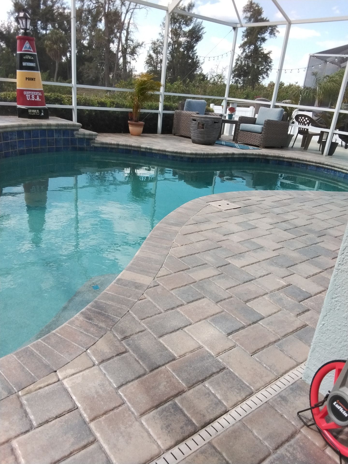 Swimming pool with blue water, brick deck, and patio seating under a screened enclosure.