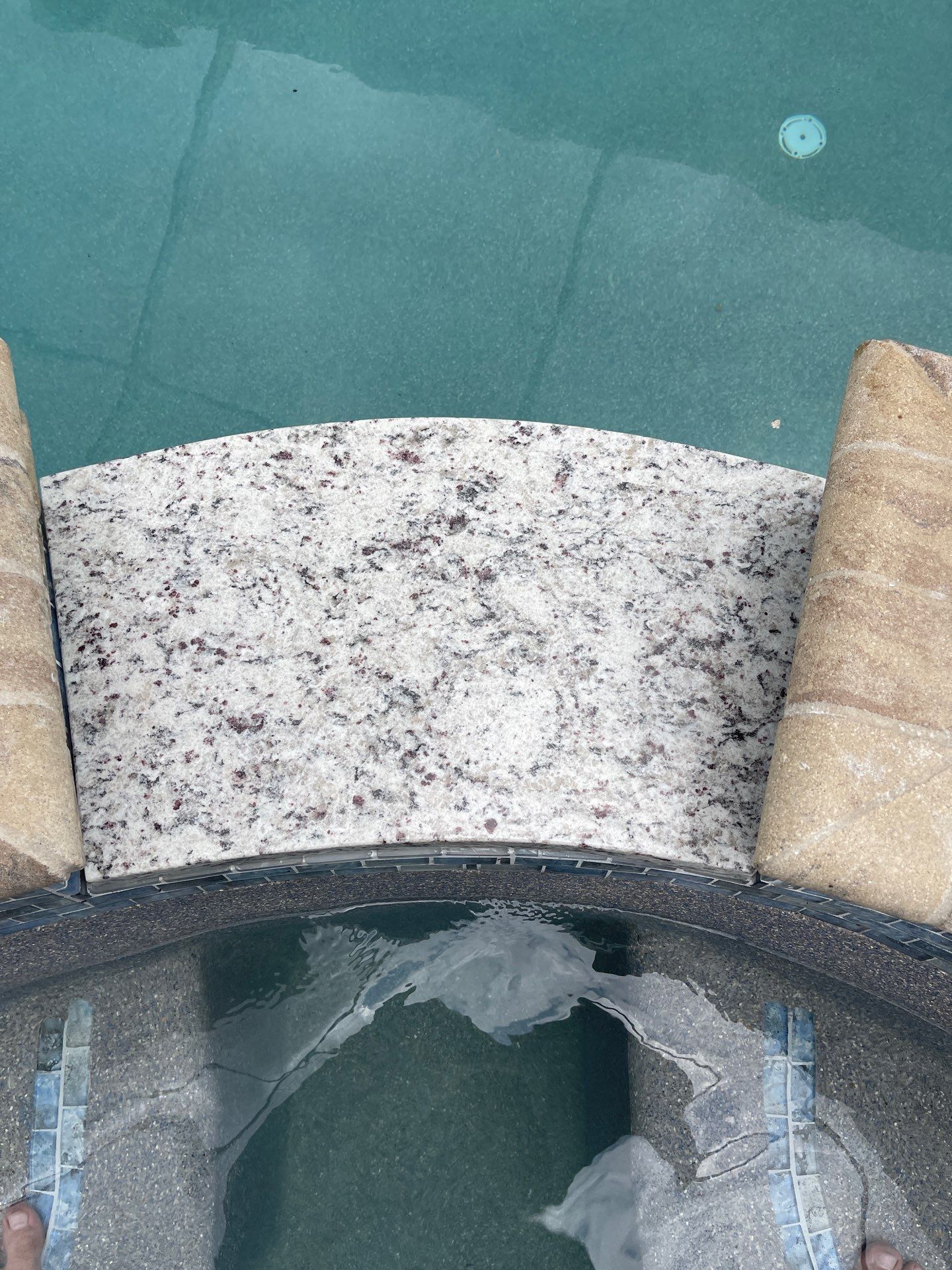 Stone pool edge with turquoise water and a circular opening below, flanked by two tan columns.