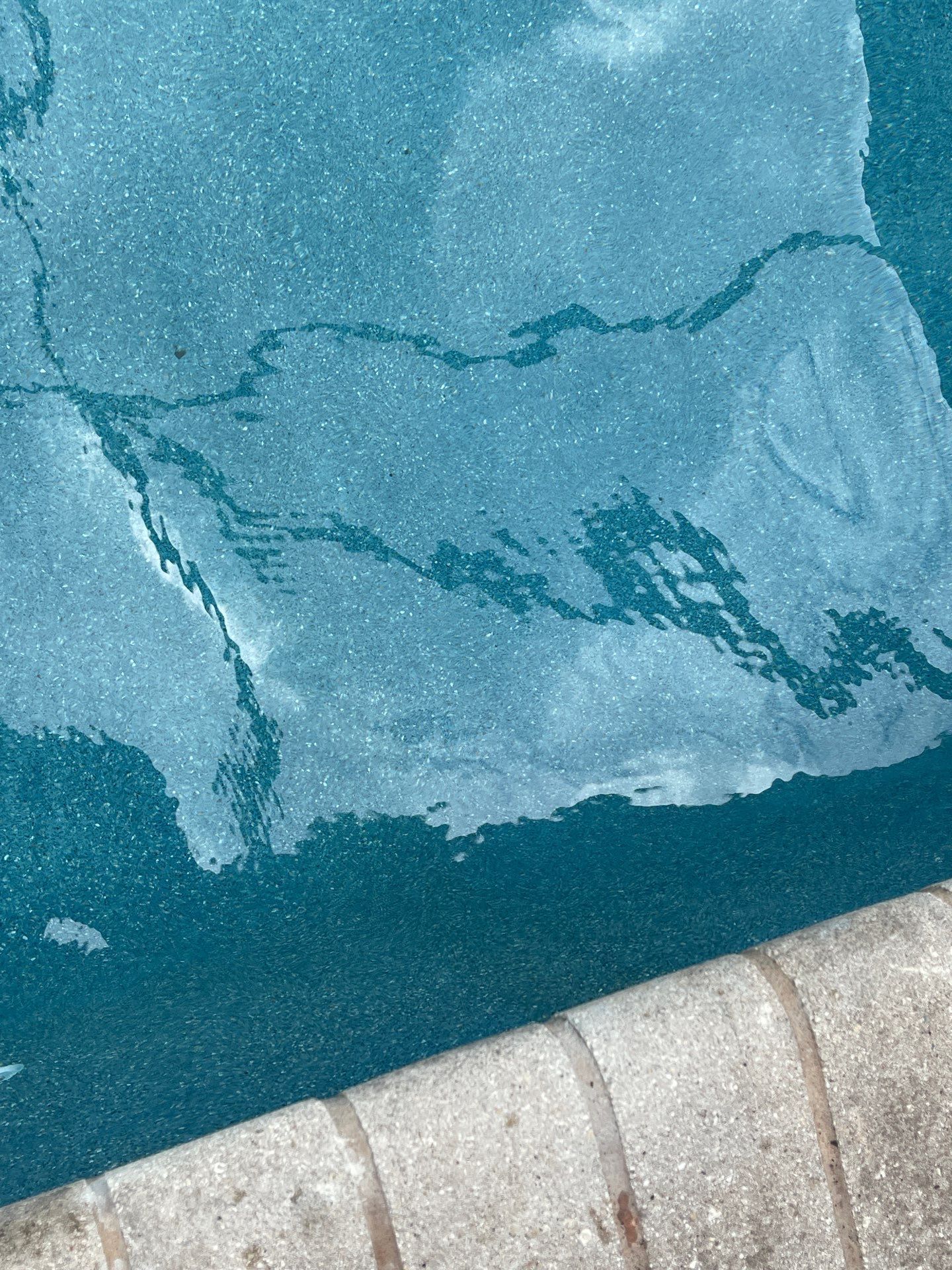Blue water with a cracked icy surface beside a concrete edge.