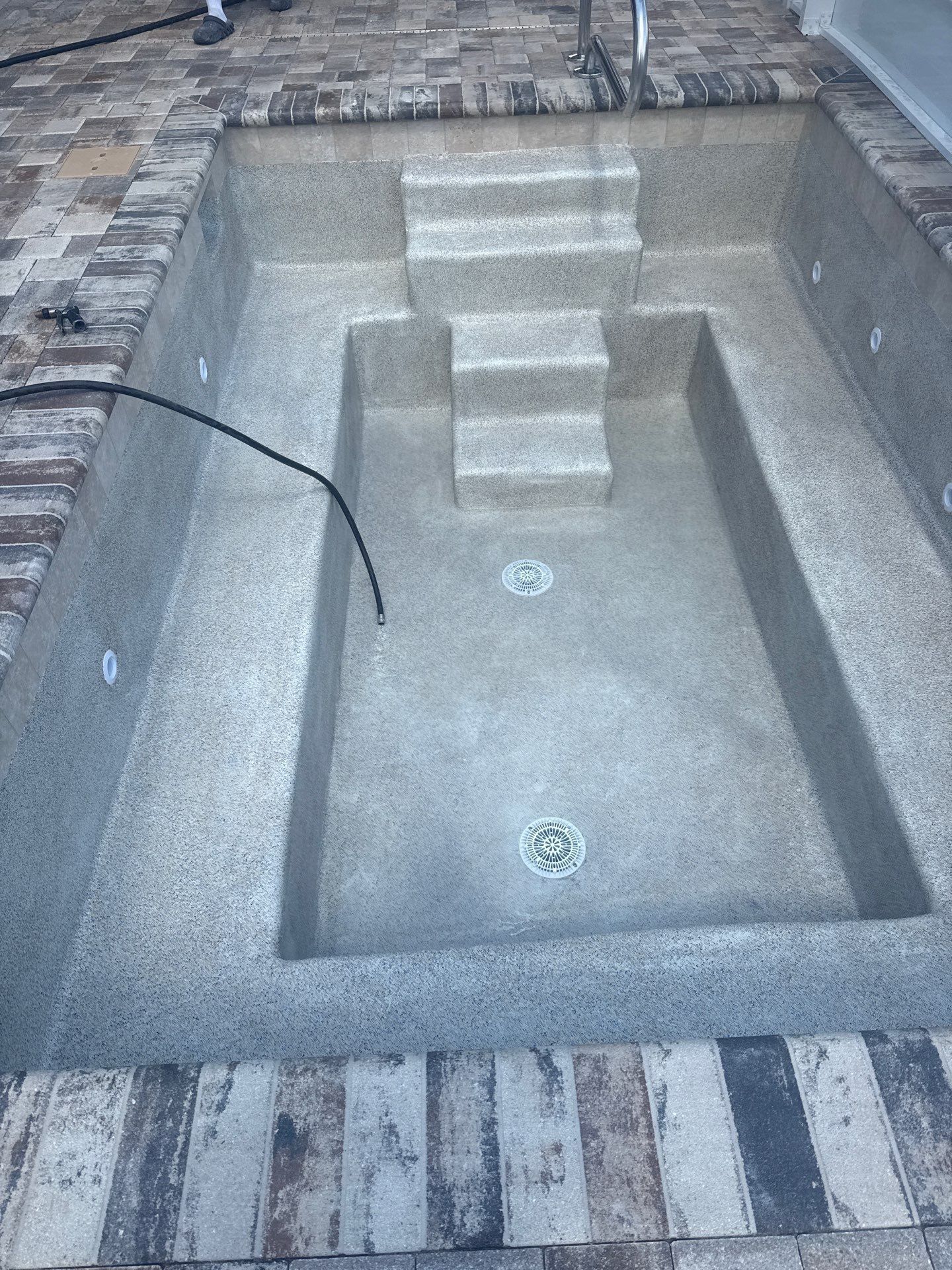 Empty concrete pool with steps and two drains, viewed from above.