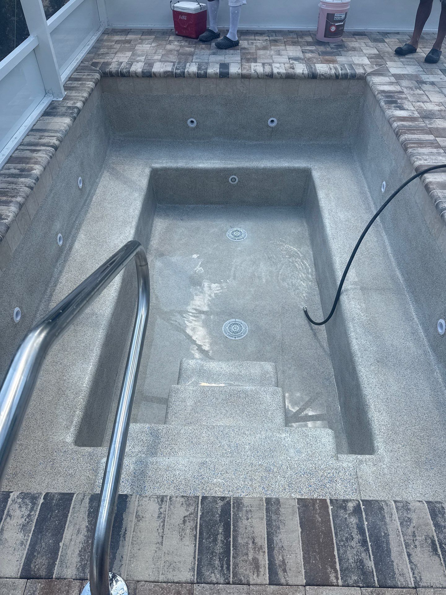 Empty concrete pool with steps, metal handrails, and a hose inside, viewed from above.