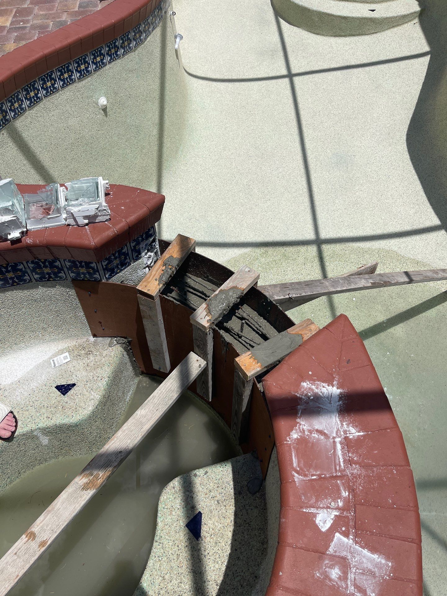 Broken red-and-gray metal bench in a tiled outdoor area, with parts bent and damaged.