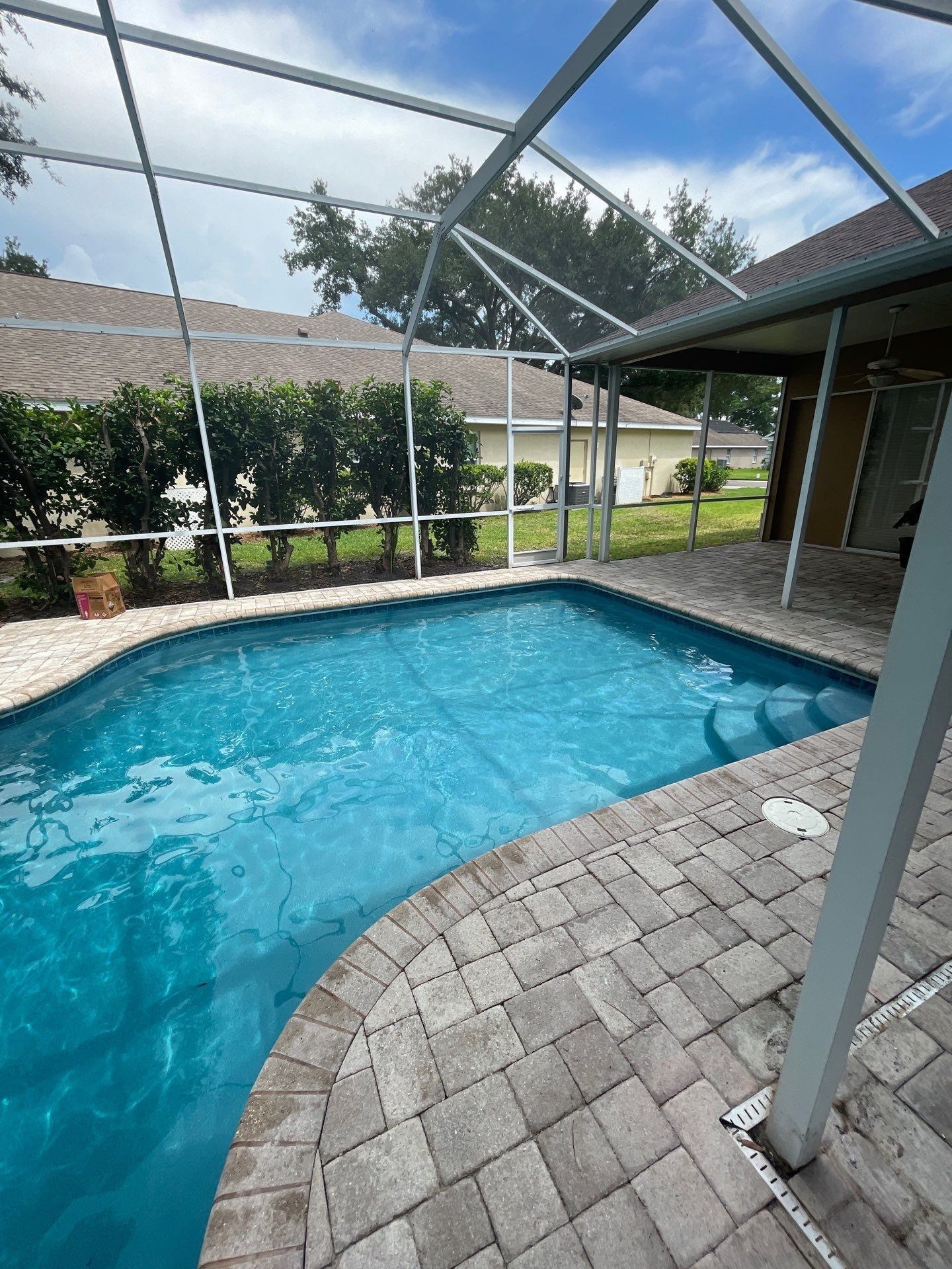 Screened-in backyard pool with blue water and a brick patio under a metal frame enclosure.