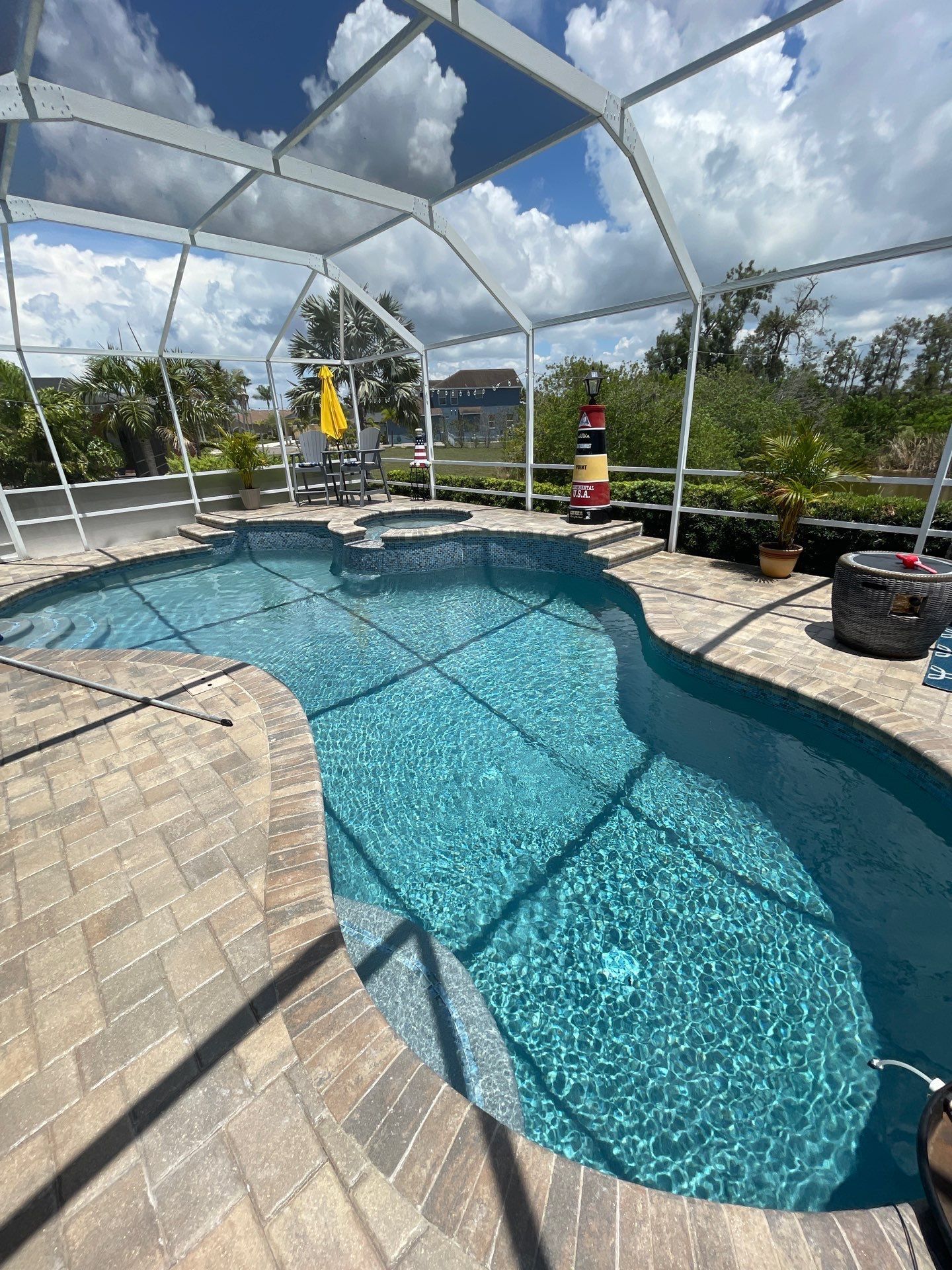 Screened backyard pool with turquoise water, tan pavers, and lounge chairs under a partly cloudy sky.