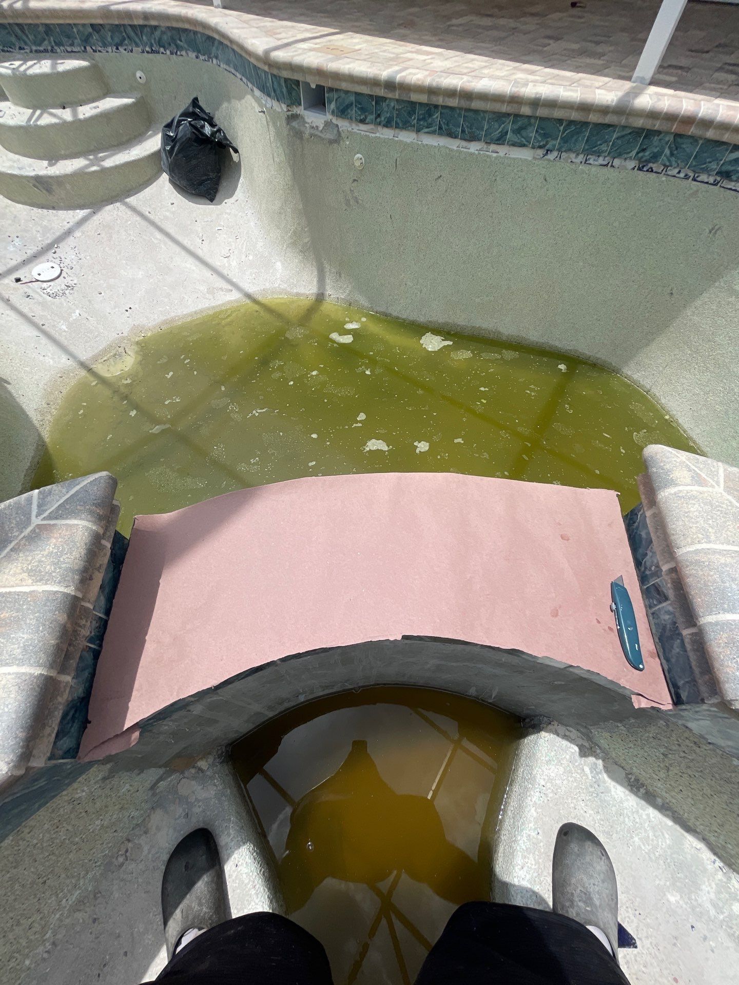 Outdoor hot tub with murky green water and pink cushions, viewed from above.