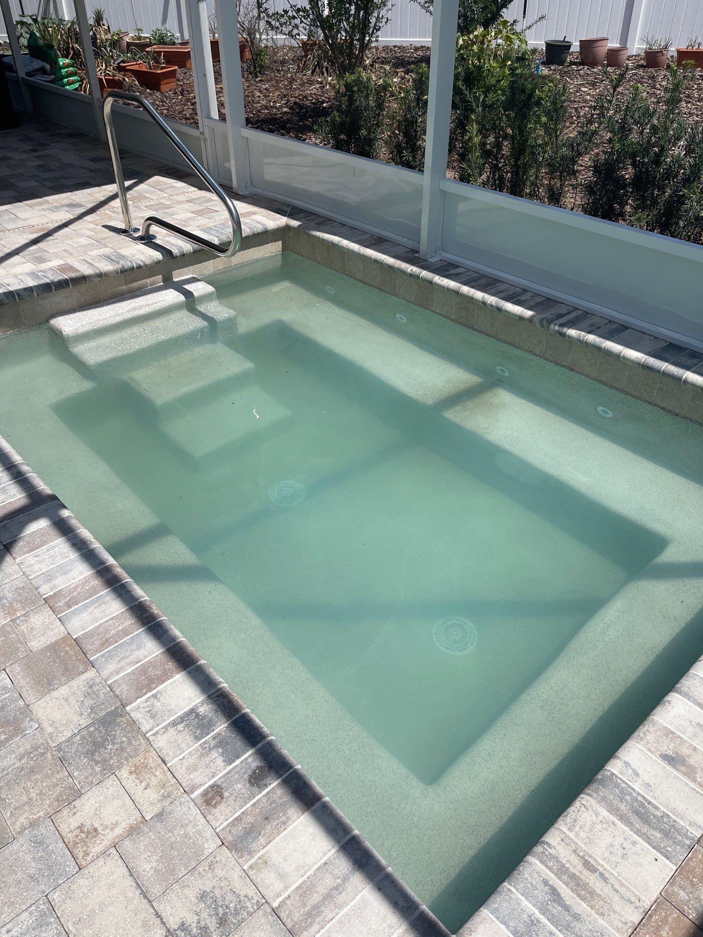 Small outdoor rectangular pool with pale green water, tiled deck, and metal handrails.