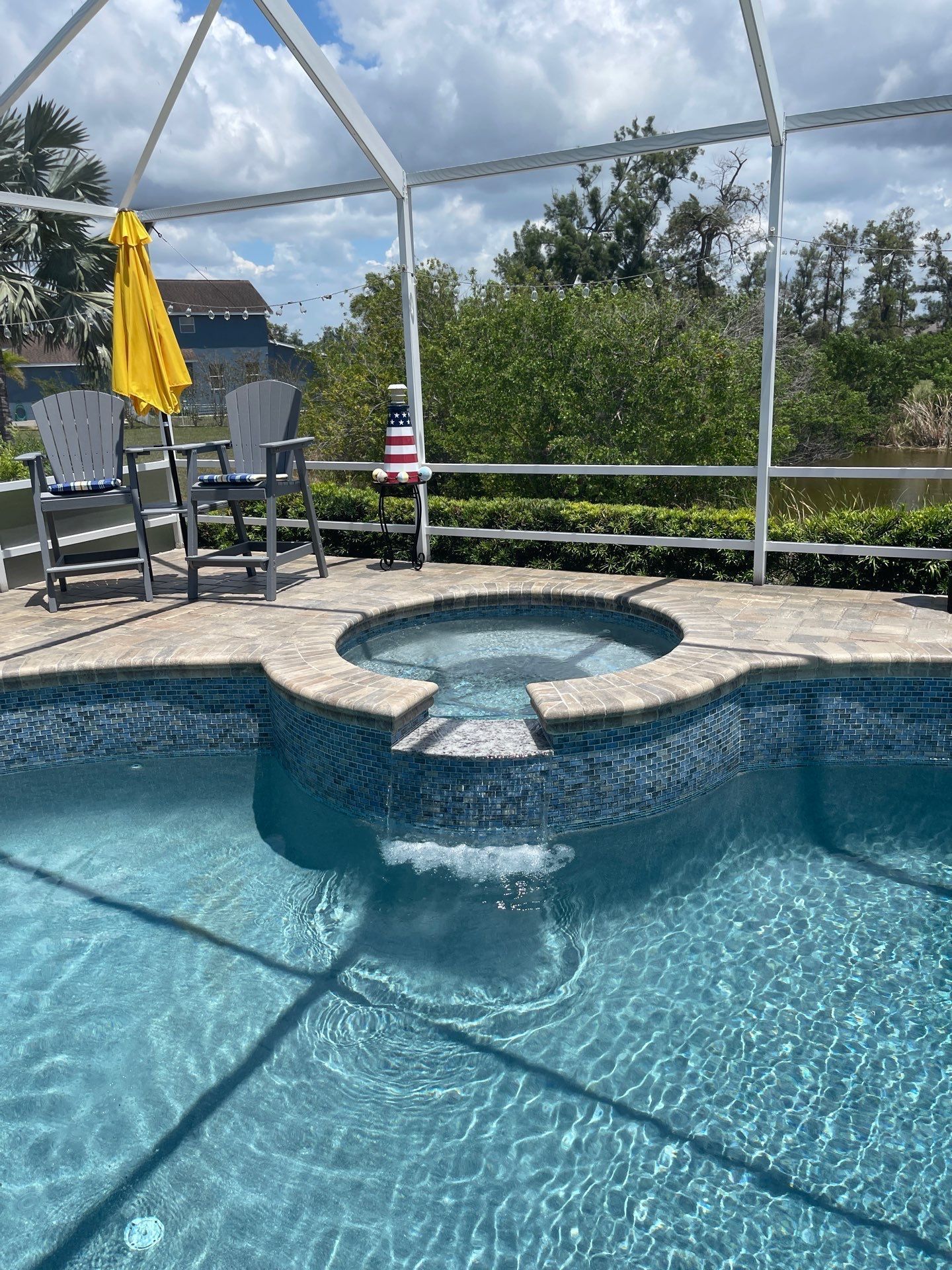 Backyard pool with spa, two lounge chairs, yellow umbrella, and screened enclosure under a blue sky.