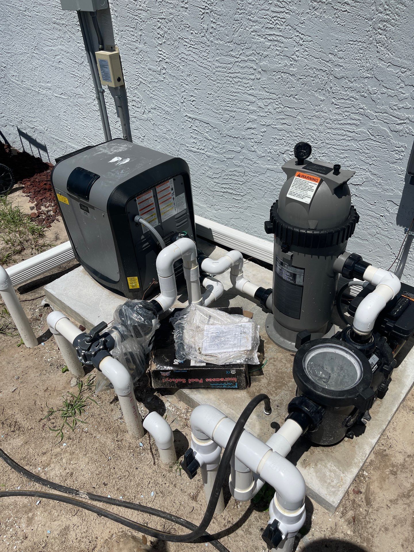 Pool pump and filtration equipment with white PVC pipes mounted beside a stucco wall.
