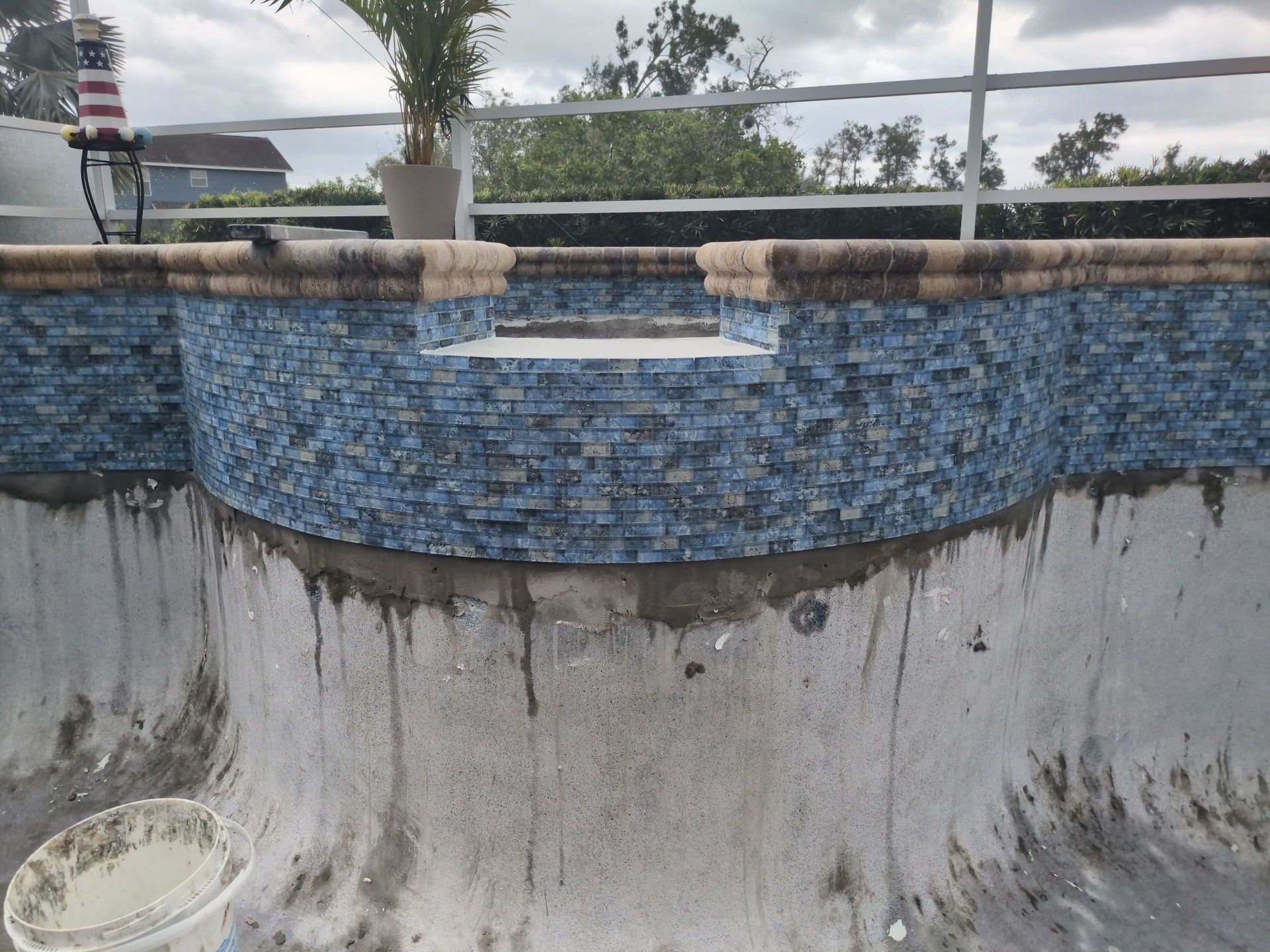 Empty mosaic-tiled pool with a small spillway and cloudy sky reflections in the waterless basin.