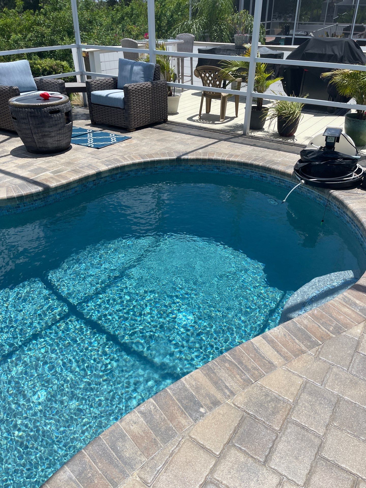 Backyard swimming pool with blue water, paver patio, and outdoor seating in sunlight.