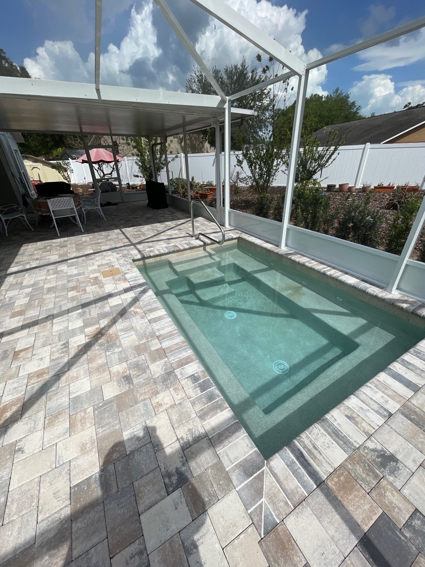 Small fenced pool with clear water under a white canopy, surrounded by light brick pavers and lounge chairs.