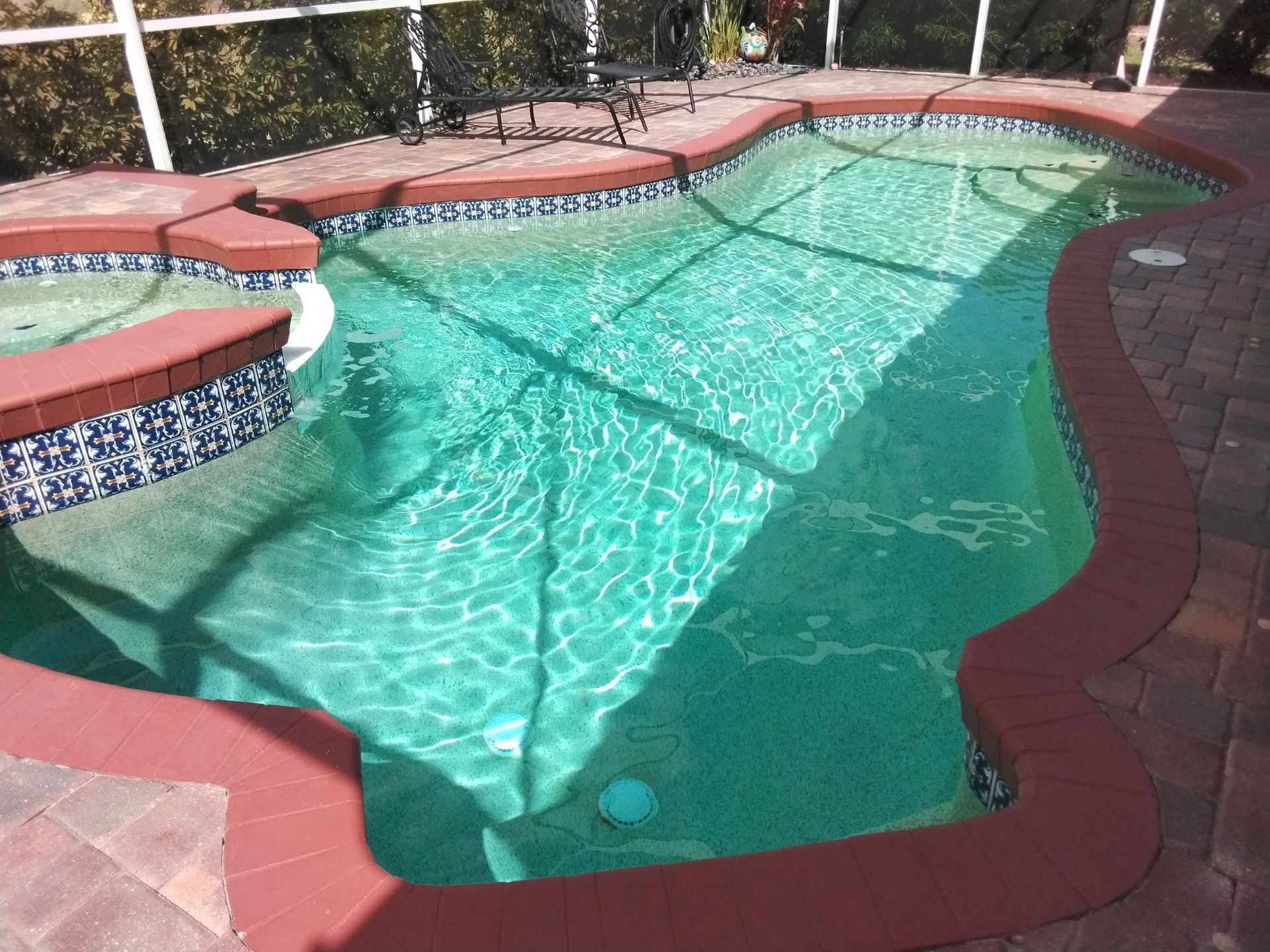 Curved backyard swimming pool with turquoise water, red brick coping, and a small raised spa area.