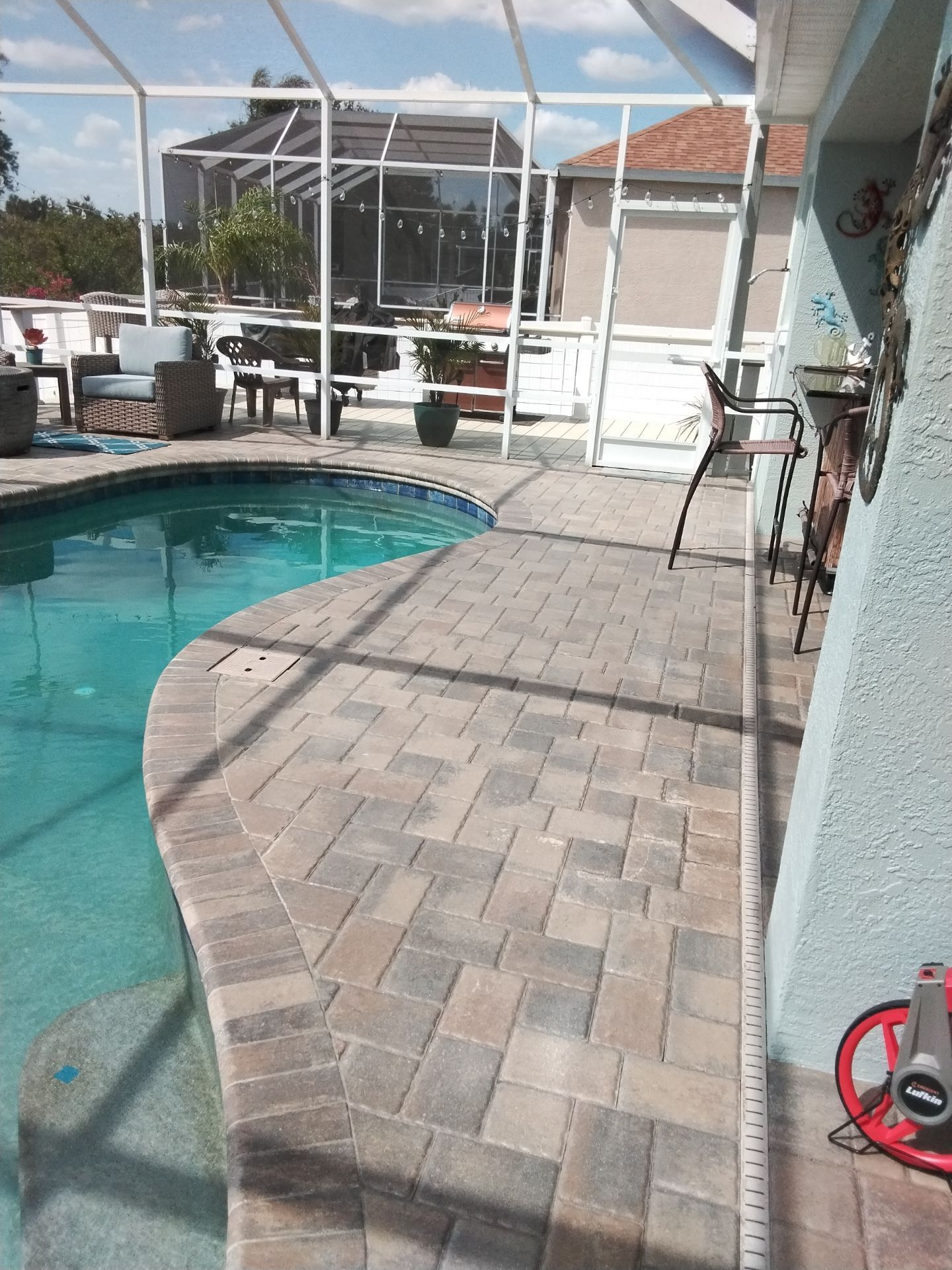 Poolside patio with curved pavers, turquoise pool water, and screened lanai in the background.