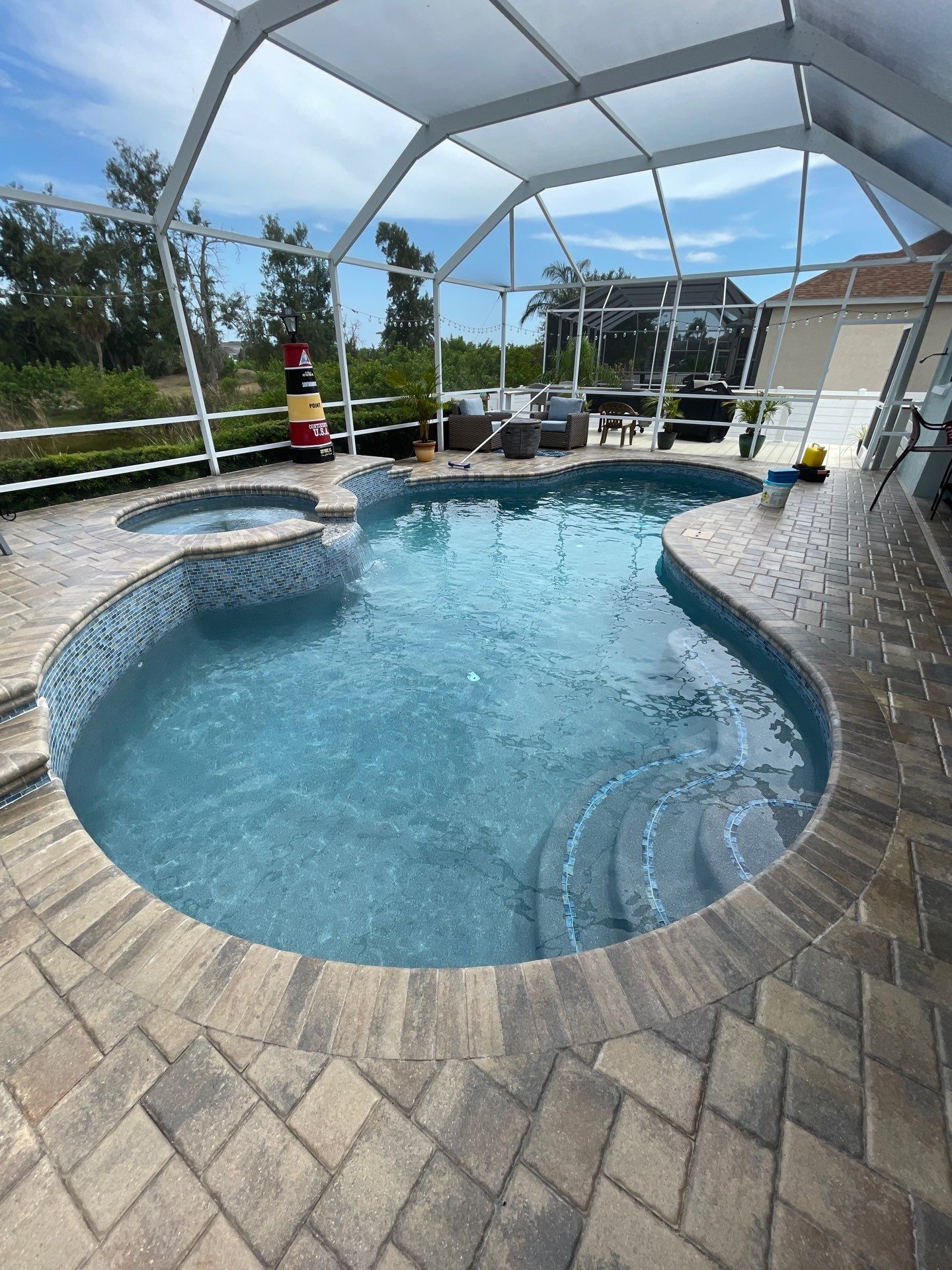 Backyard pool with curved stone deck, screened enclosure, and blue sky overhead.