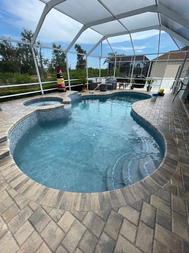 Screened backyard pool with spa, curved steps, and stone patio under a white enclosure.