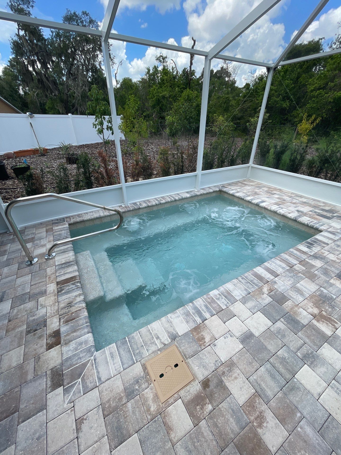 Small tiled hot tub with clear water on a screened patio, surrounded by pavers and greenery.