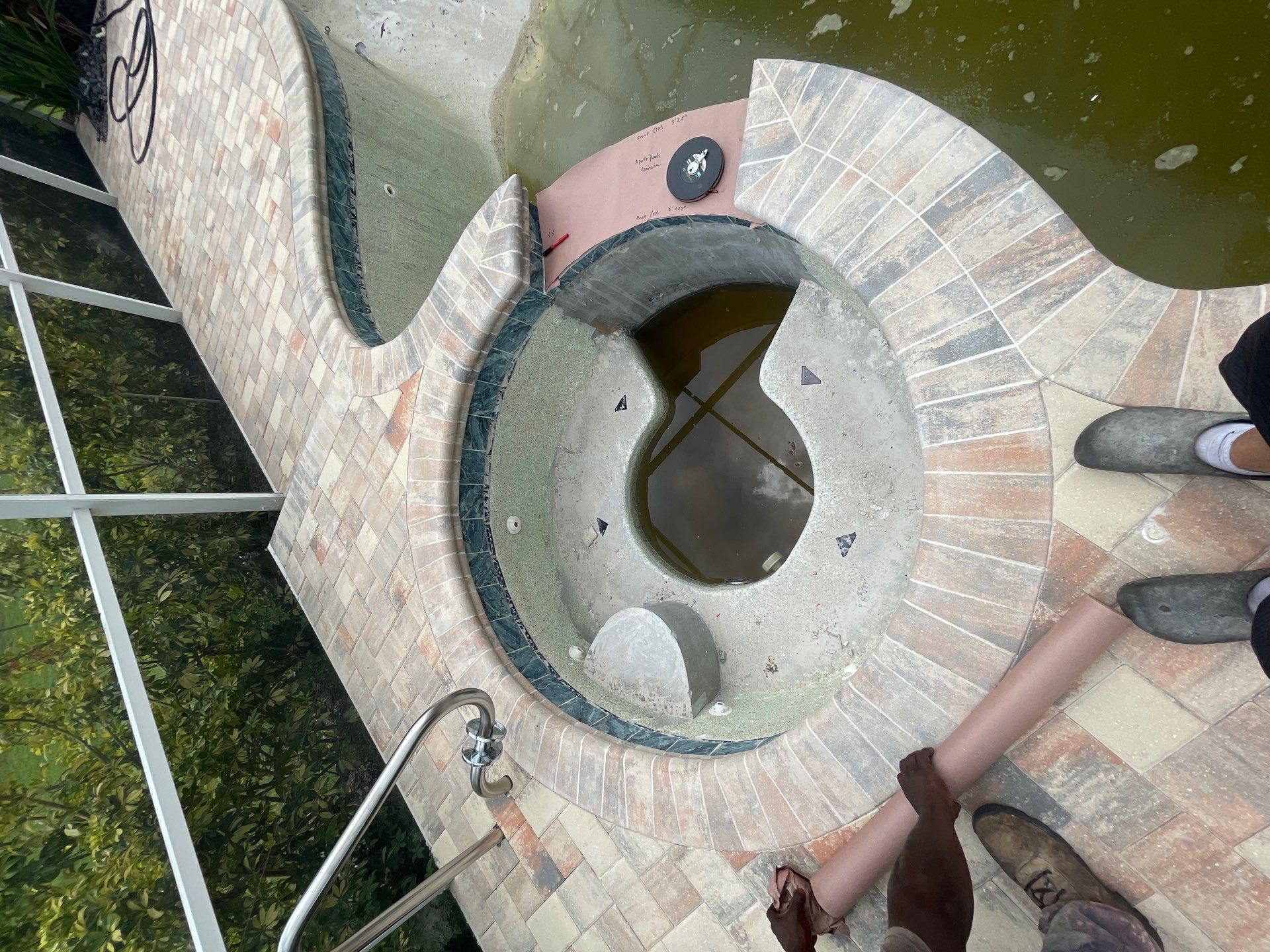 Stone spiral fountain with a circular basin and green water, viewed from above.