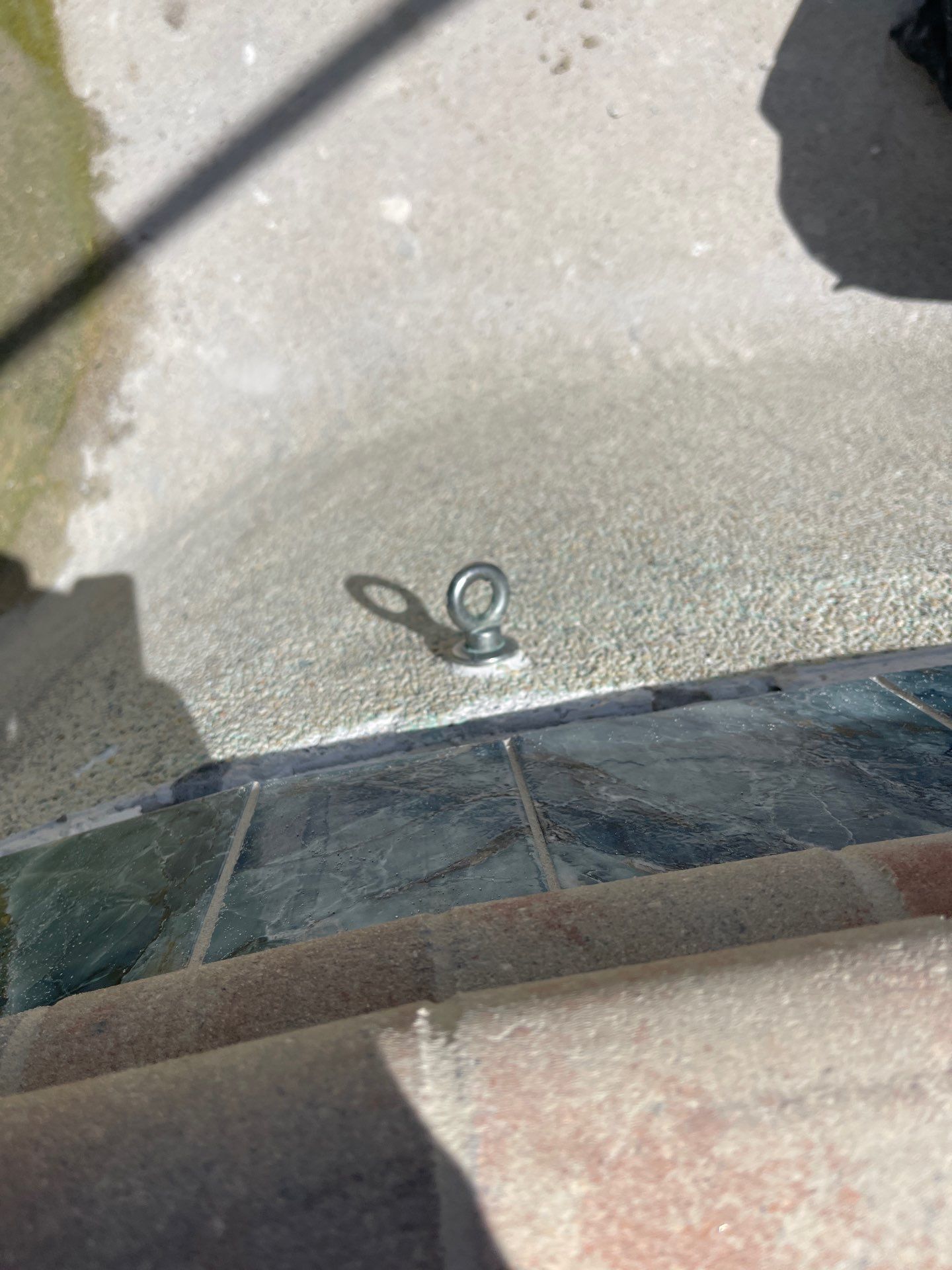 Small pair of scissors on a concrete surface beside a car bumper, with sunlight and shadows.