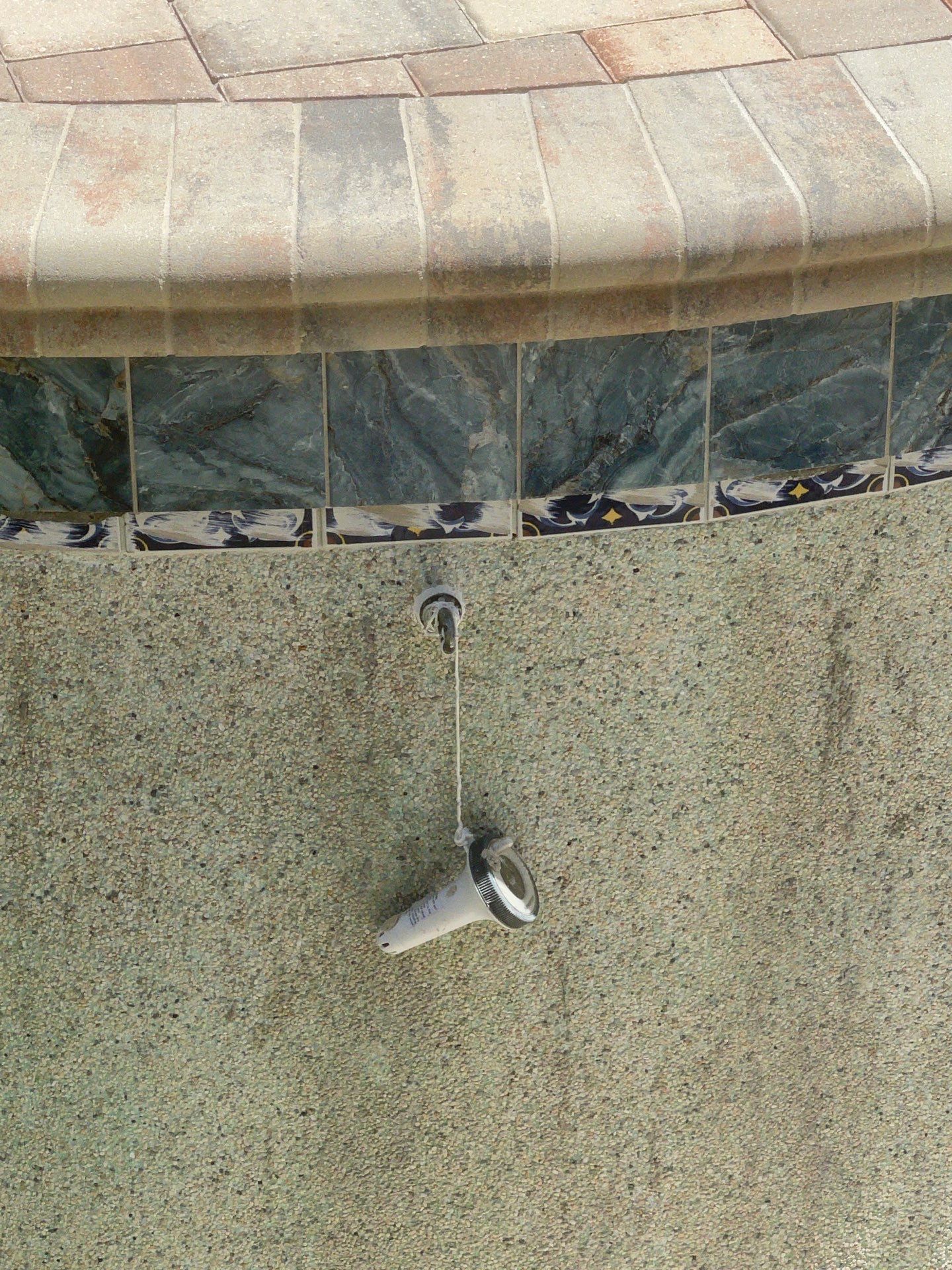A black outdoor shower head on a beige stucco wall beneath a tiled ledge.